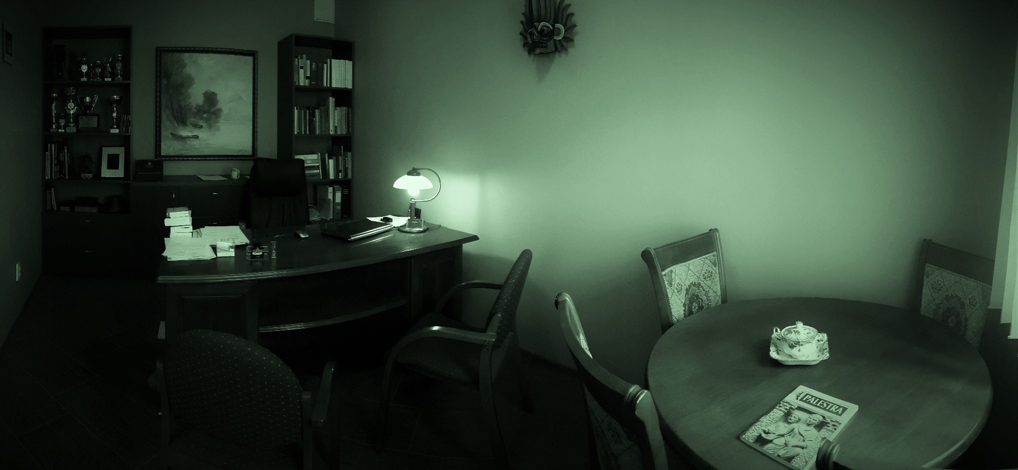 Klimatyczne wnętrze kancelarii prawnej z biurkiem, regałem z książkami i stołem z czasopismem 'Palestra'. Uwagę zwraca stonowana kolorystyka i elegancki wystrój.