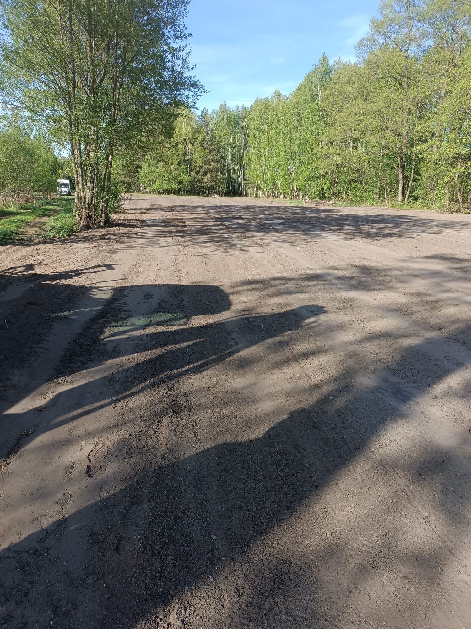 Utrwardzony teren pod budowę, widoczne ślady opon i drzewa w tle. Przygotowany grunt pod inwestycję z zachowaniem naturalnego otoczenia.