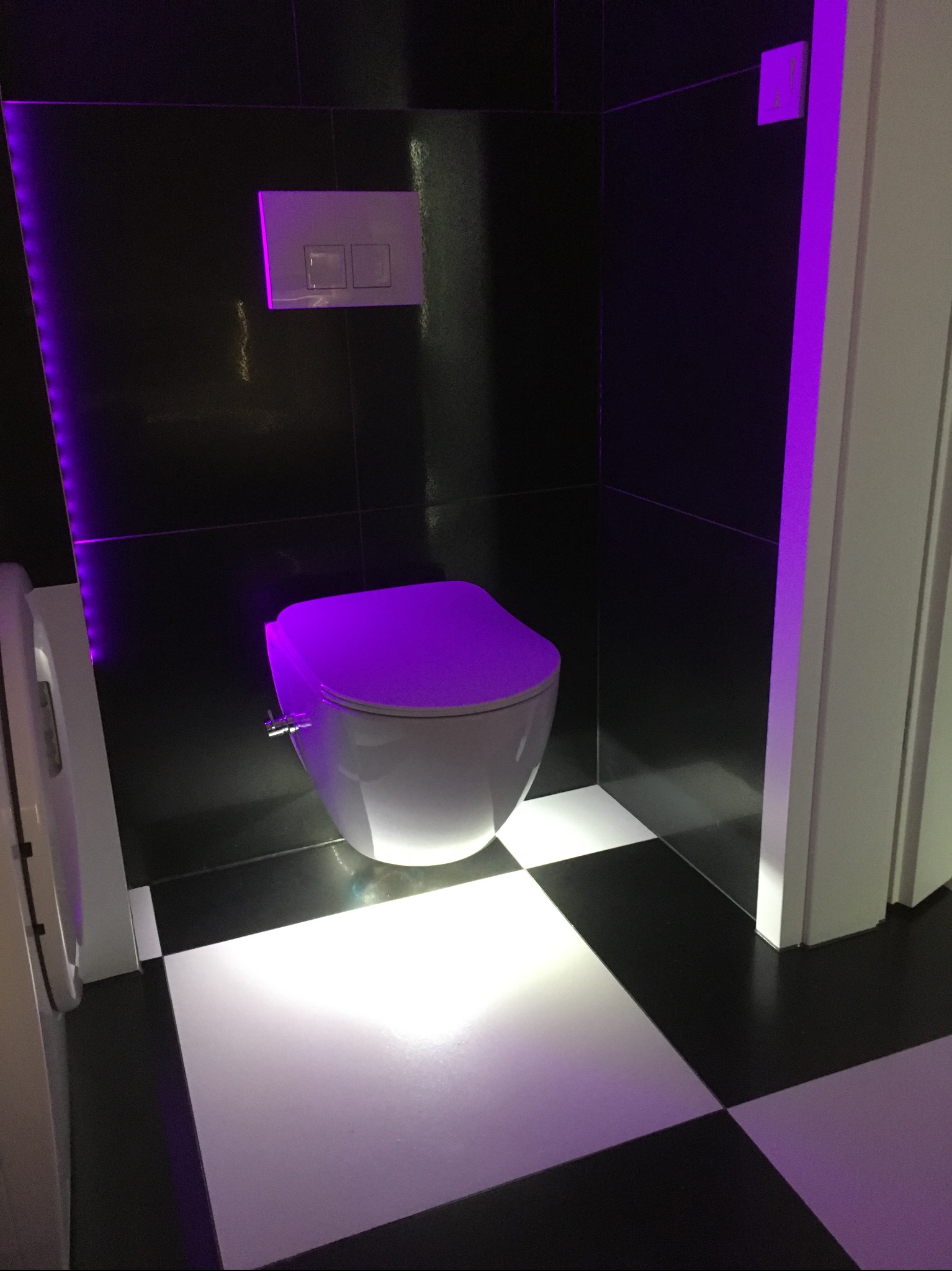 Nowoczesna łazienka z toaletą w geometryczne wzory płytek podświetlona fioletowym światłem LED. Kontrast czerni i bieli.