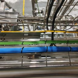 I-Markon - Kompleksowa instalacja kablowa w Szczecinie z przewodami w kolorach: niebieskim, zielonym i żółtym, zamocowanymi na metalowej konstrukcji. Widok z dołu.