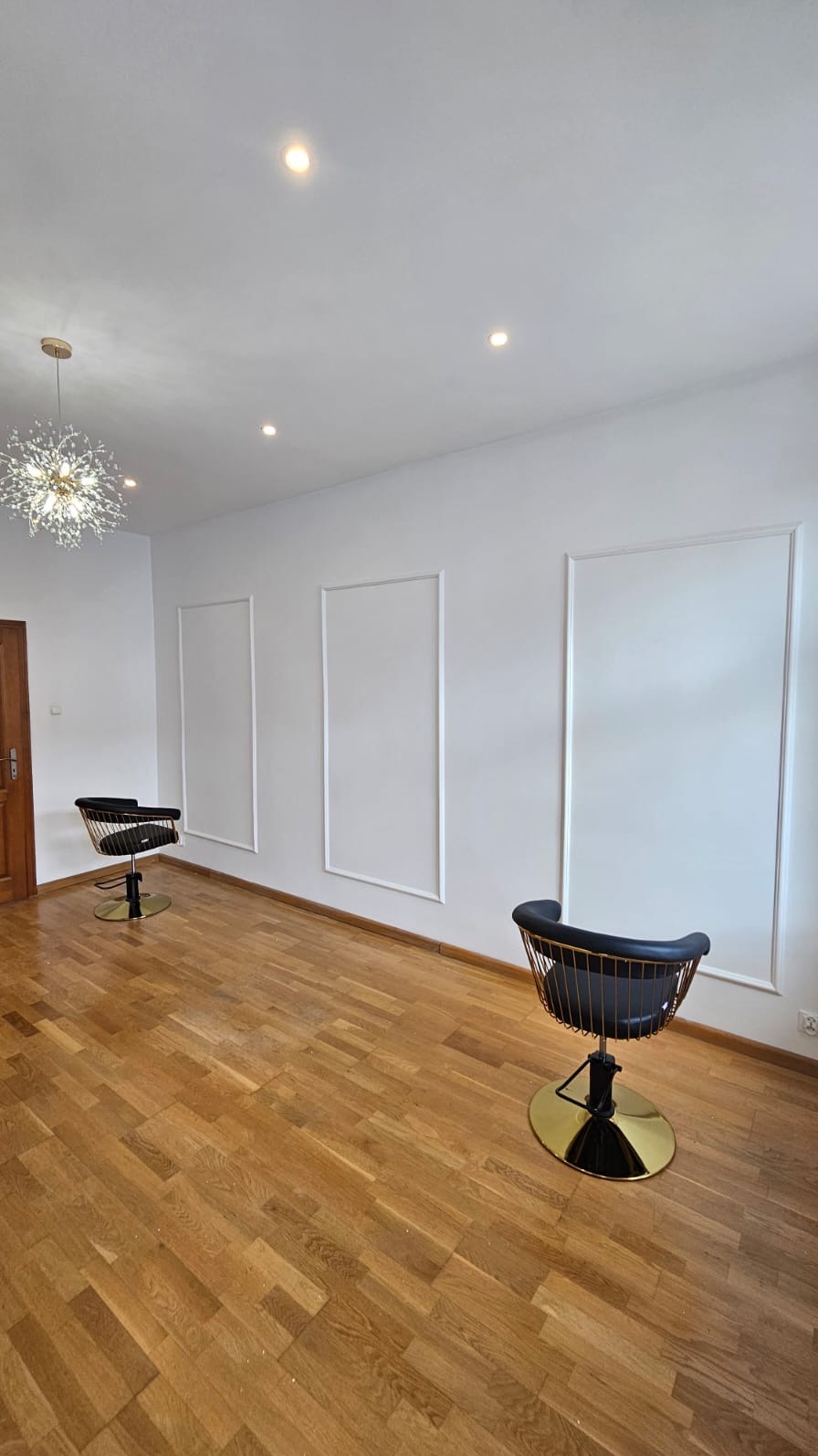 Nowoczesne oświetlenie LED i dekoracyjne listwy ścienne w jasnym wnętrzu z dwoma krzesłami fryzjerskimi na drewnianej podłodze.