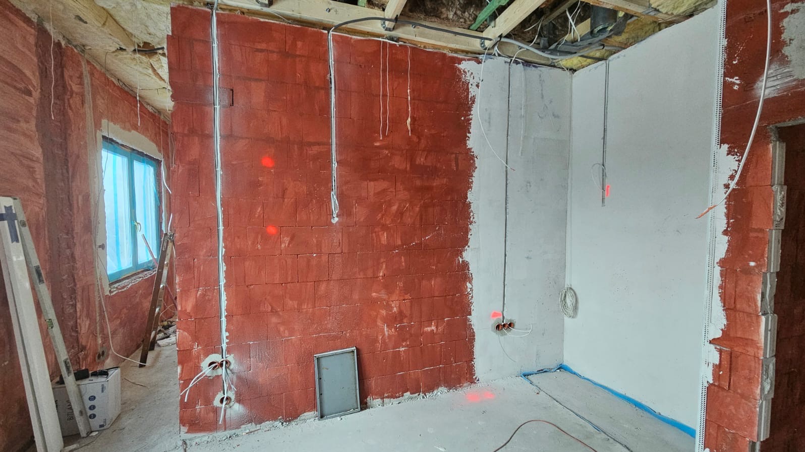 Wnętrze w trakcie prac wykończeniowych: ściany z instalacją elektryczną, częściowo otynkowane, z widocznymi przewodami i puszkami. Surowy stan, przygotowanie do dalszych prac.