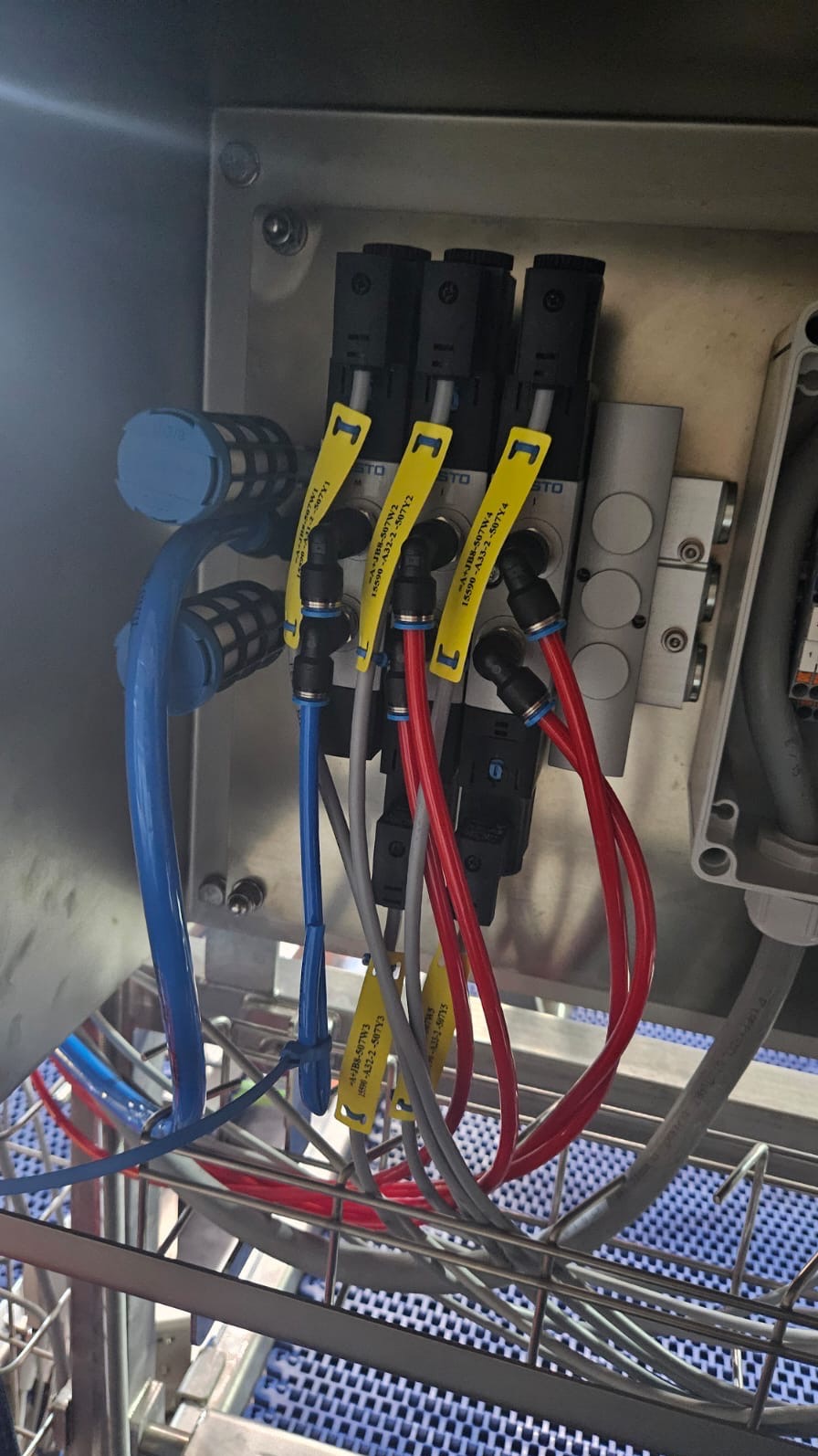 Kompleksowy układ pneumatyczny z czarnymi zaworami Festo, żółtymi etykietami i kolorowymi przewodami w metalowej obudowie, część przemysłowej instalacji. Precyzyjne połączenia.