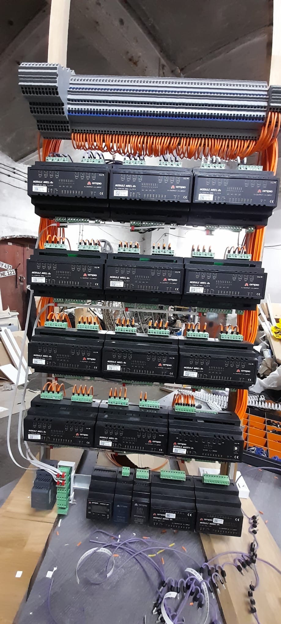 Rozbudowana szafa sterownicza z modułami Ampio MREL-8, pomarańczowymi kablami i listwami zaciskowymi. Widok z dołu na instalację w trakcie montażu.
