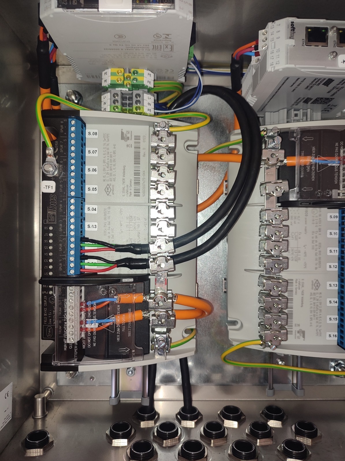 Panel sterowniczy z widocznymi modułami, przewodami i złączkami. Precyzyjny montaż instalacji w metalowej obudowie. Widoczne oznaczenia i etykiety na komponentach.