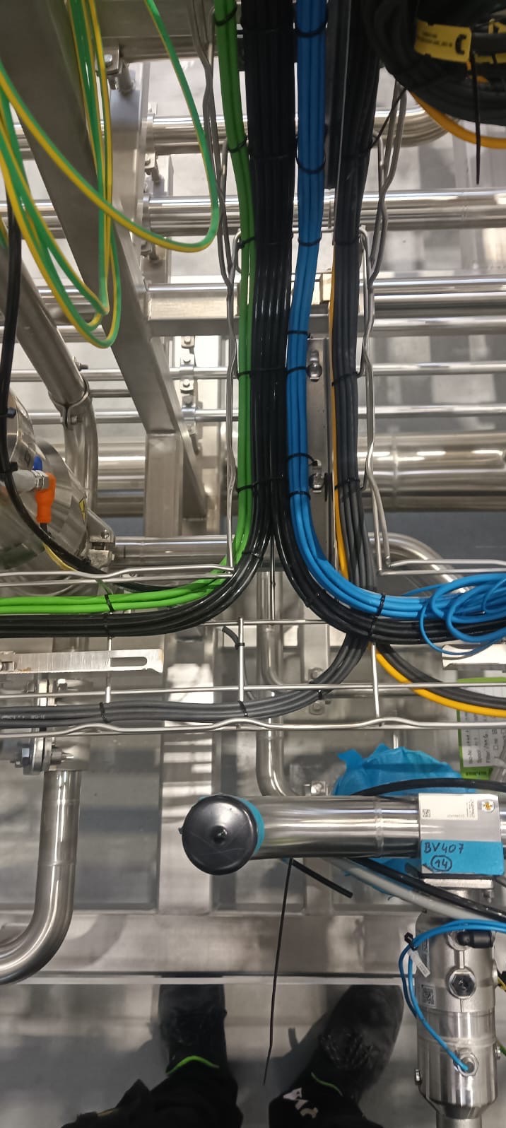 Profesjonalnie ułożone, kolorowe kable elektryczne w metalowej konstrukcji, zabezpieczone opaskami zaciskowymi. Widoczne rury i elementy instalacji.