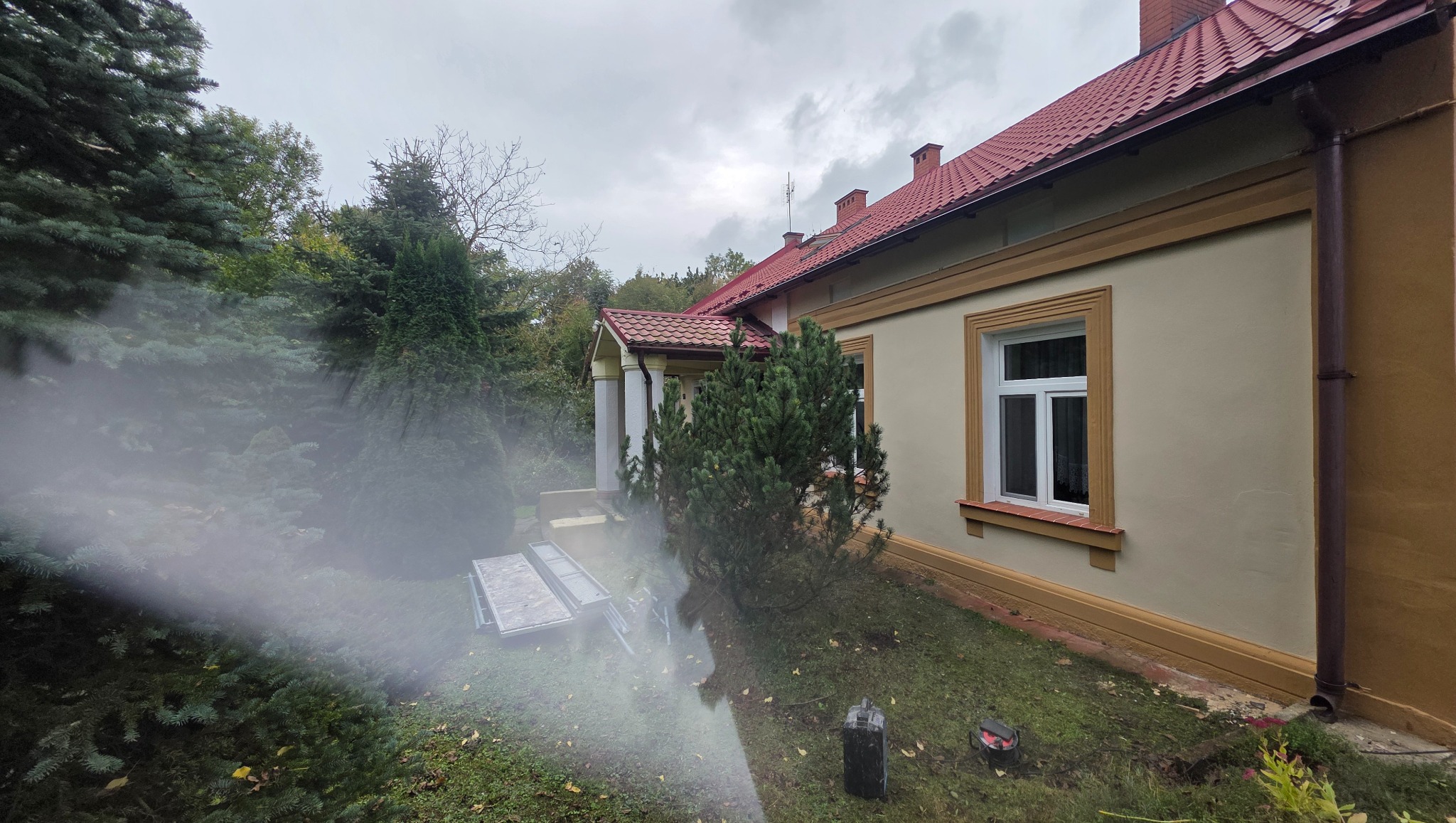 Czyszczenie elewacji domu jednorodzinnego za pomocą myjki ciśnieniowej. Widoczne rusztowania i elementy elewacji po czyszczeniu.