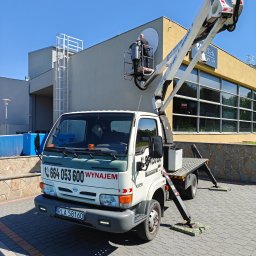 KASPOL Ireneusz Kaszowski - Podnośnik koszowy KASPOL na tle budynku z szyldem restauracji, pracownik w koszu na wysokości, mycie okien lub montaż reklamy, błękitne niebo.