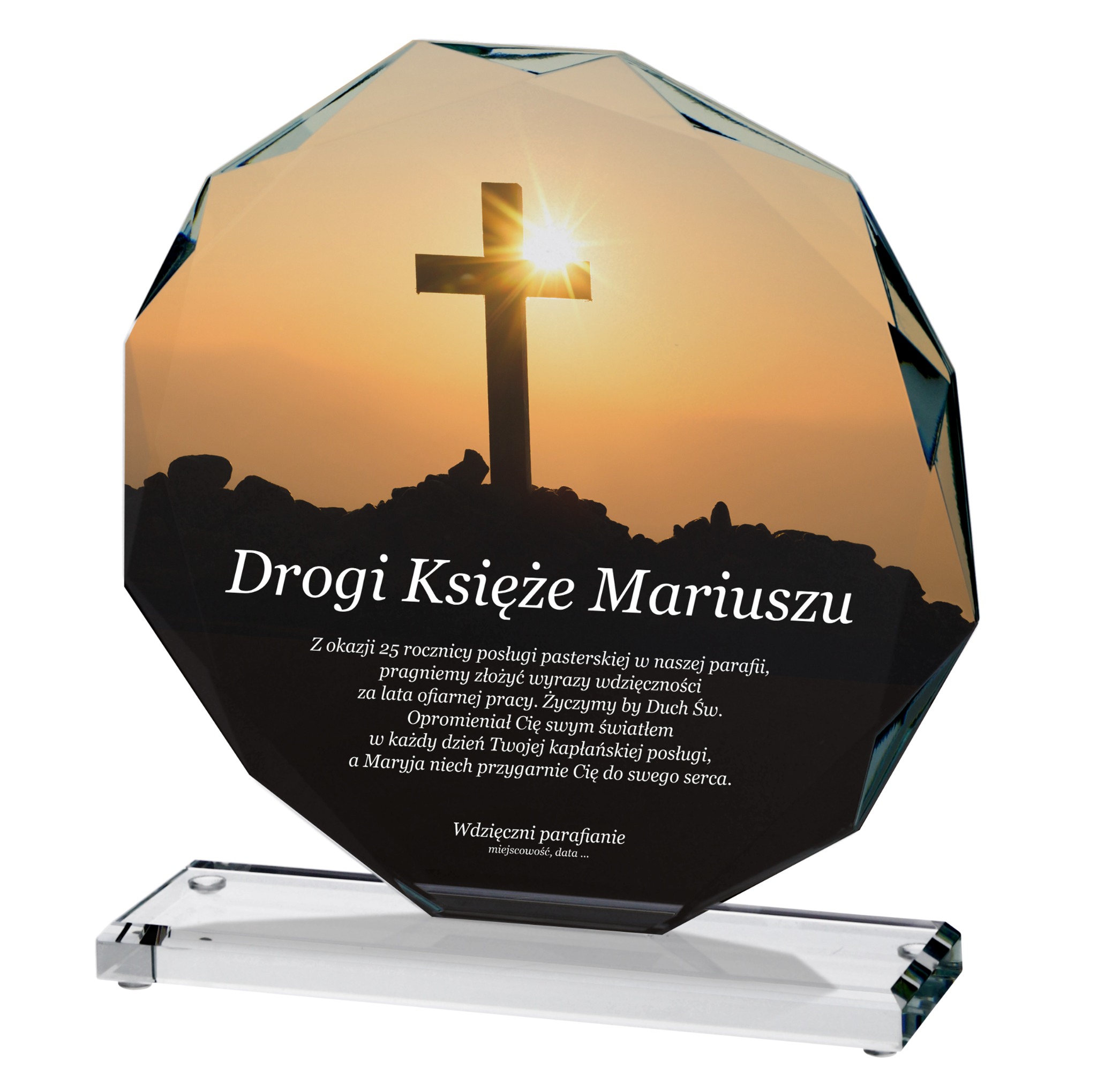 Szklana statuetka z motywem krzyża i dedykacją dla Księdza Mariusza, idealna jako podziękowanie lub jubileuszowy upominek. Widoczny zachód słońca w tle.