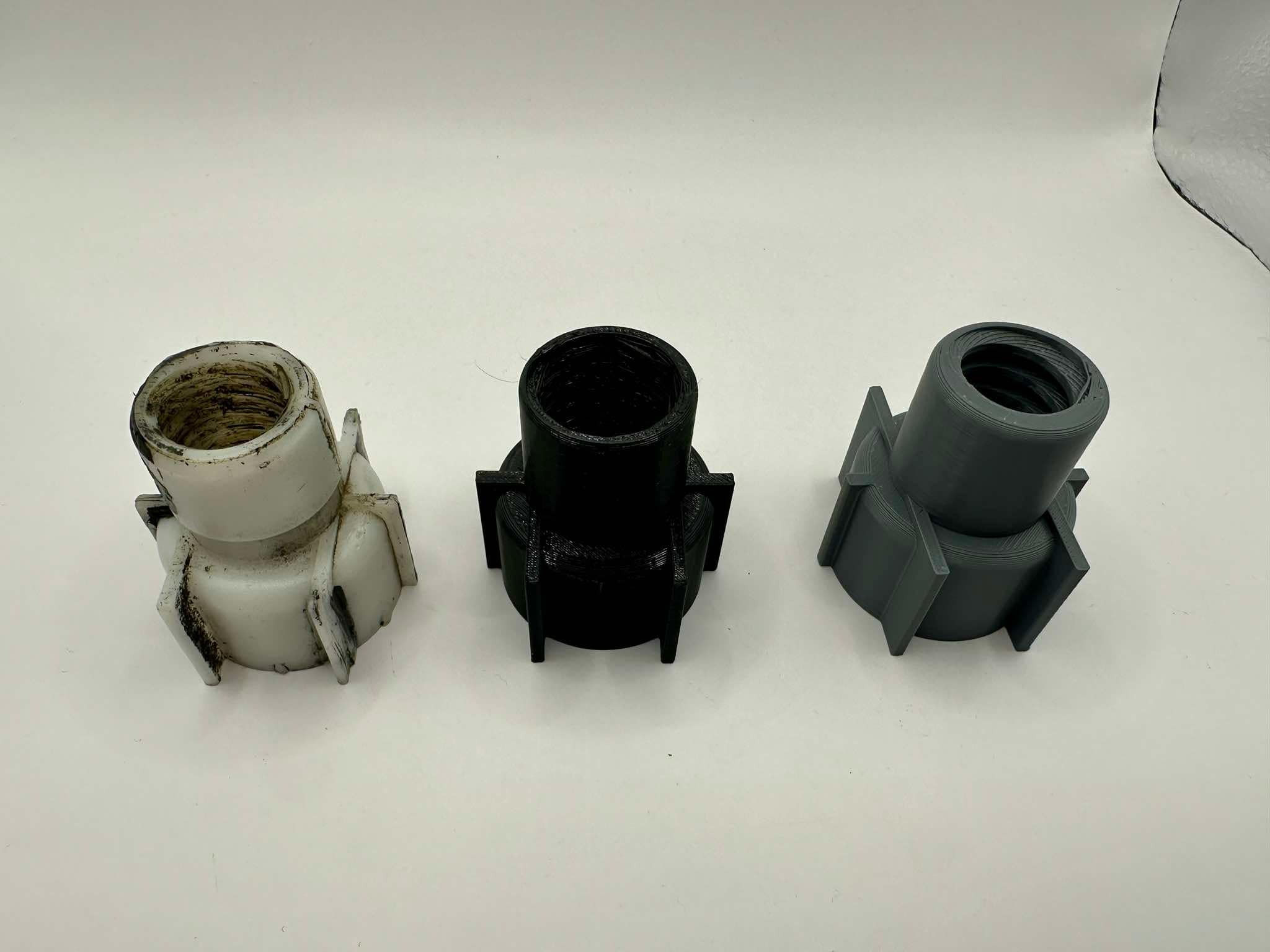 Trzy złącza rurowe, białe używane, czarne i szare, wydrukowane 3D, leżą na białym tle, prezentując różne etapy użytkowania i kolory materiałów.