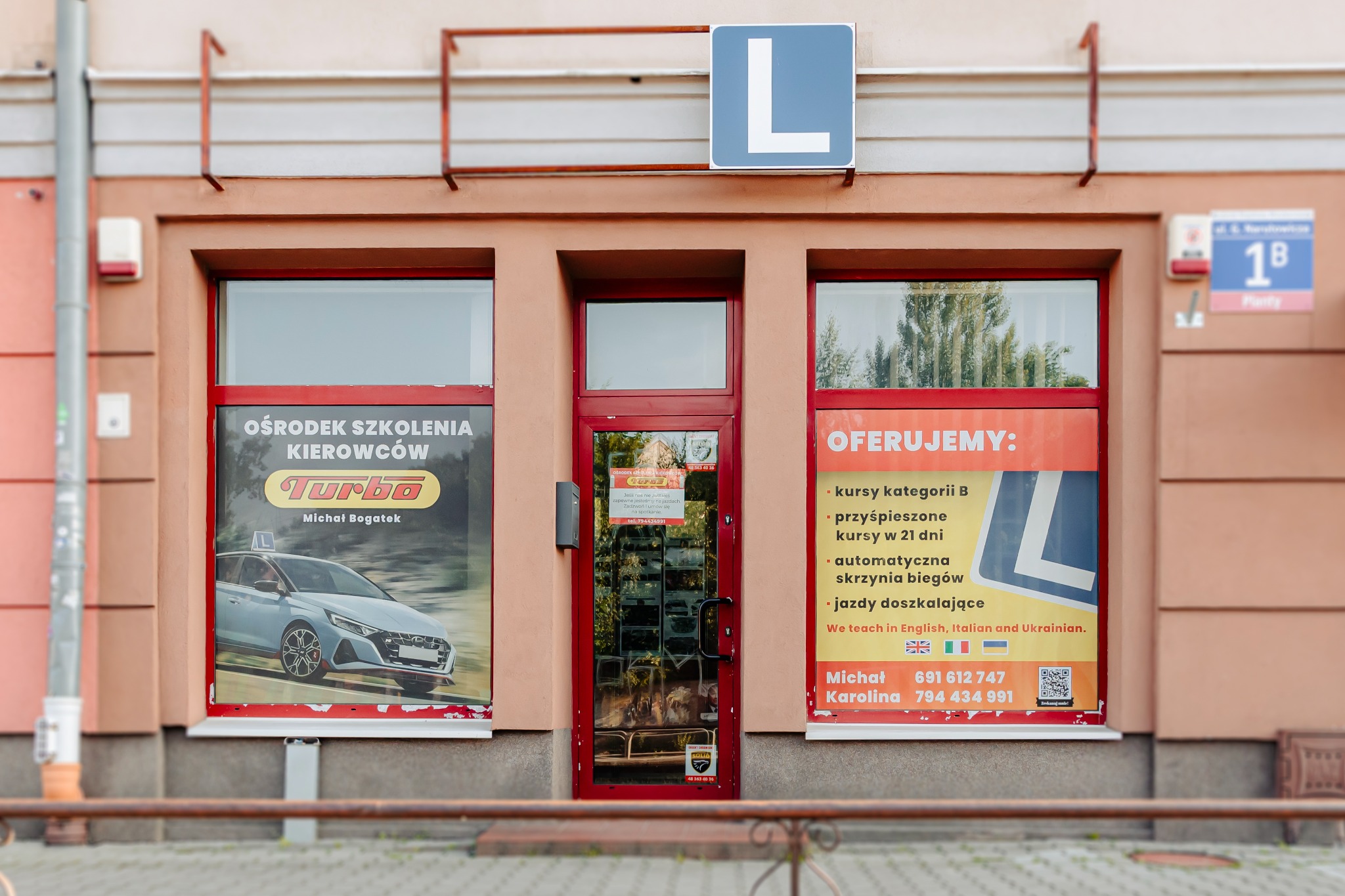 Fasada szkoły jazdy 'Turbo' w Radomiu z plakatem kursów kat. B, przyśpieszonych kursów i doszkalania. Widoczny znak 'L' i numer telefonu.