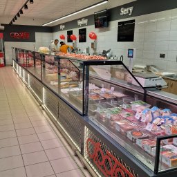 3TF Arkadiusz Szyndlarewicz - Długa, podświetlana witryna chłodnicza z różnorodnymi produktami mięsnymi i wędliniarskimi w sklepie. Widoczny personel i dekoracje balonowe.