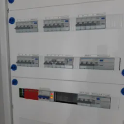 Rozdzielnica elektryczna z bezpiecznikami różnicowoprądowymi i wyłącznikiem głównym. Widoczne opisy obwodów: 'Różnicowy A, B, C, D, E', 'Indukcja', 'Garaż'.