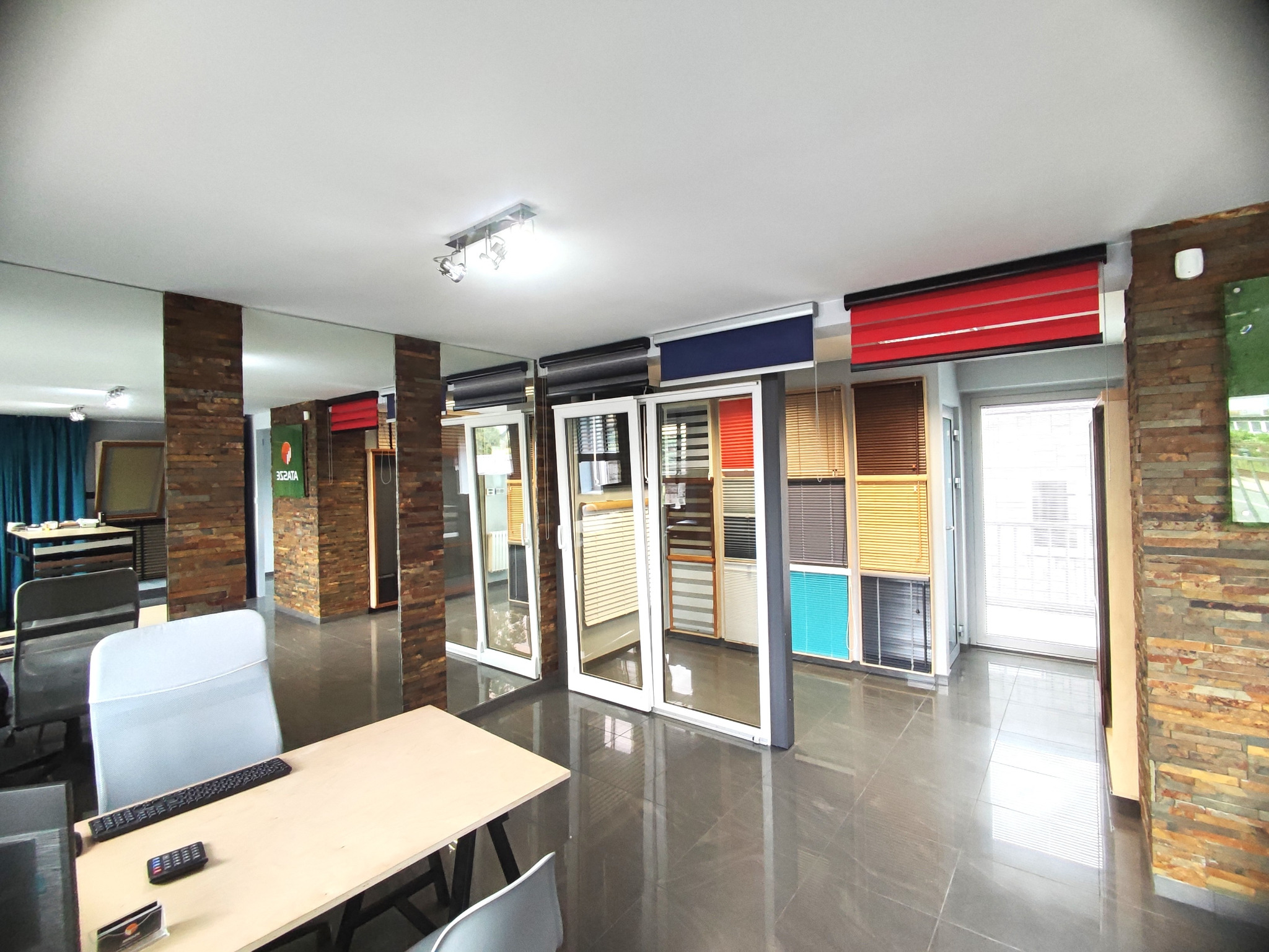 Ekspozycja różnorodnych rolet i żaluzji w salonie: rolety dzień noc, aluminiowe, drewniane. Widoczne próbki kolorów i faktur. Stonowana kolorystyka wnętrza.