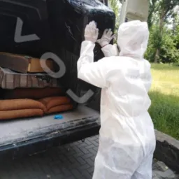 Pracownik w kombinezonie ochronnym wkłada zapakowany mebel do furgonetki. W tle widoczne inne meble i drzewa. Usługa opróżniania.