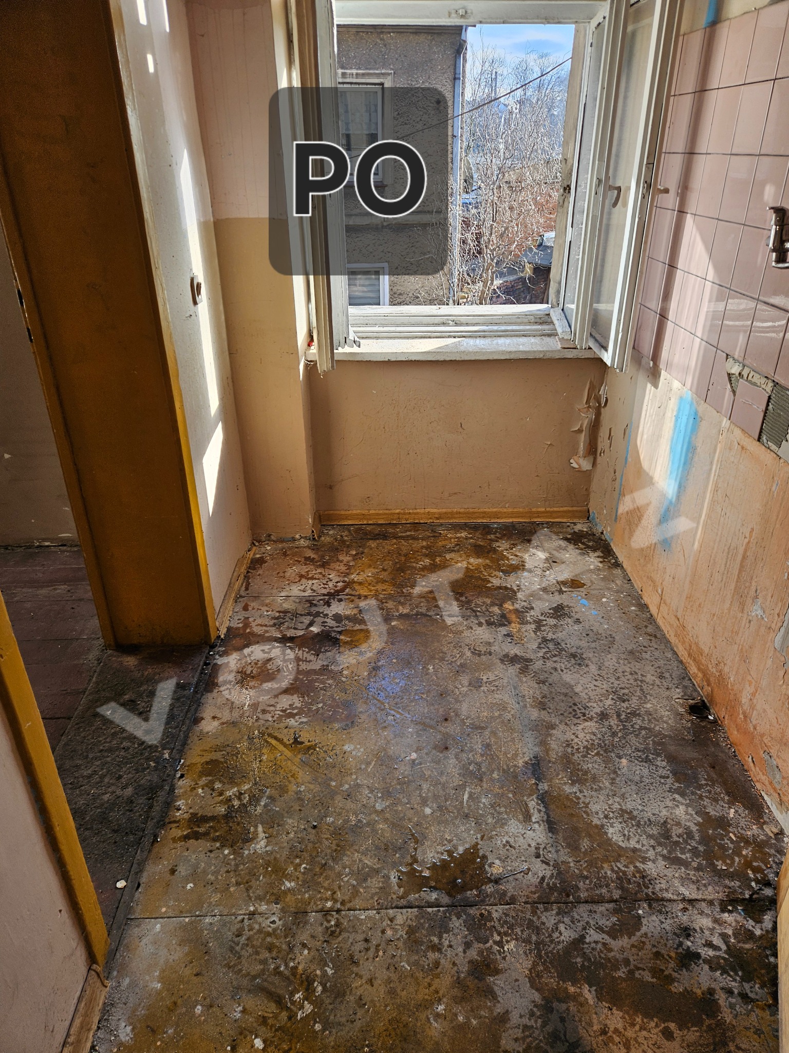 Zniszczone wnętrze po opróżnianiu: brudna podłoga, resztki na ścianach, otwarte okno. Widoczny napis 'PO' sugerujący etap końcowy prac.
