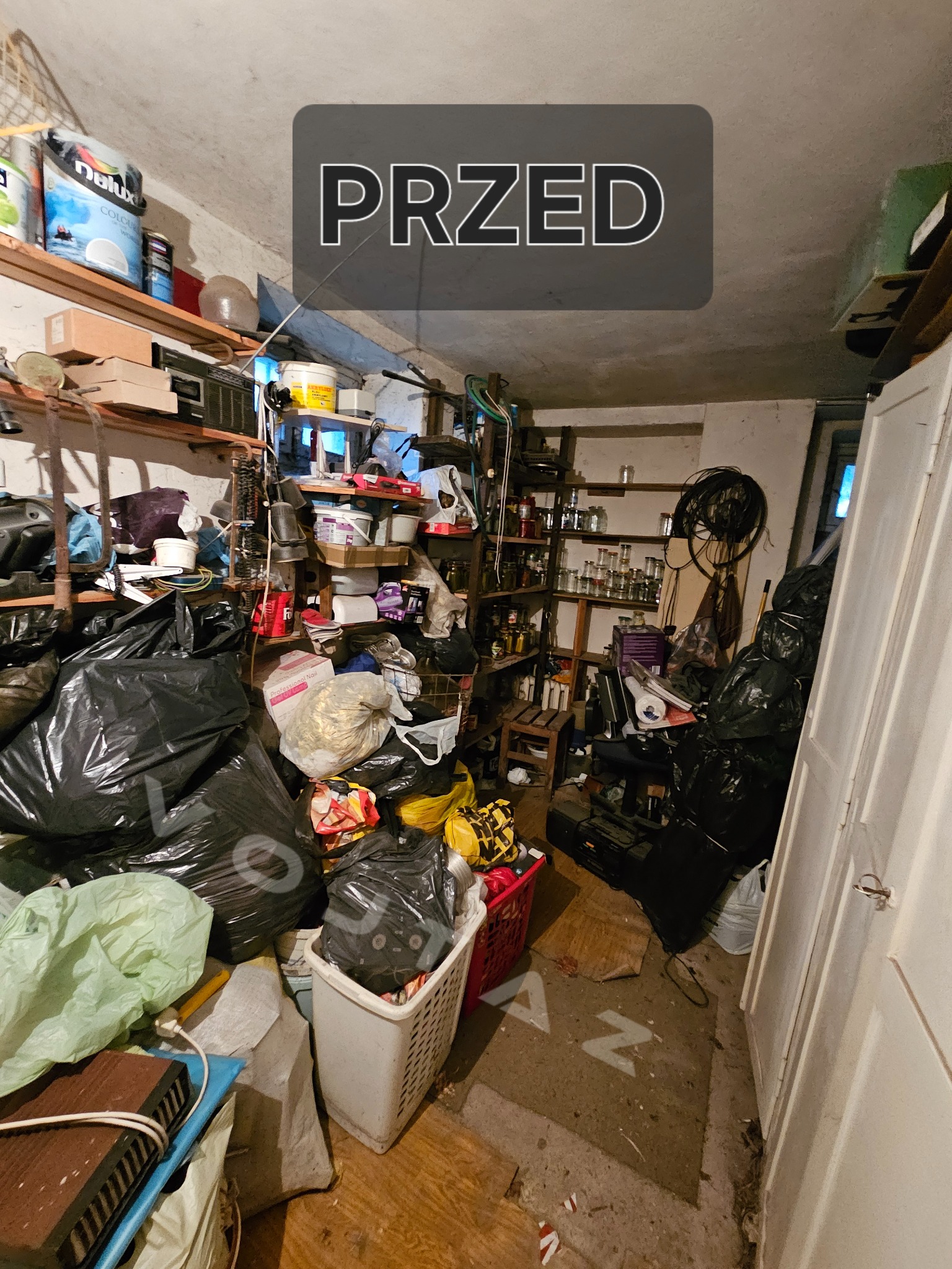 Zagracone pomieszczenie przed opróżnianiem: worki na śmieci, pudełka i przedmioty na półkach. Na podłodze widoczny napis 'PRZED'.