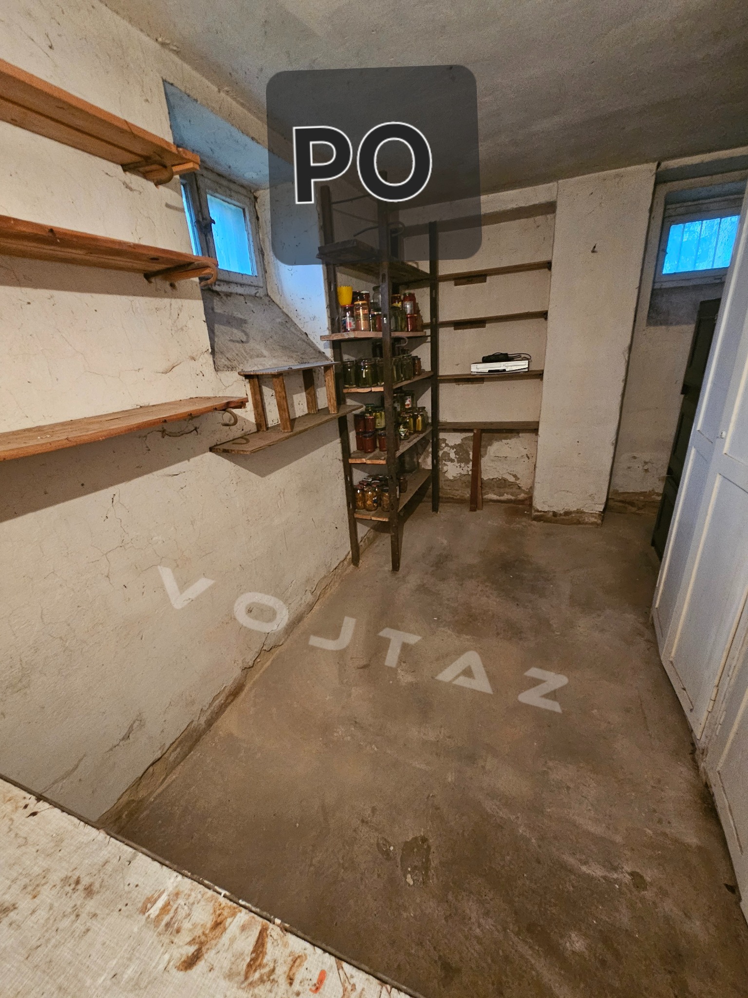 Piwnica po opróżnieniu: półki na ścianach, regał z przetworami, okno z niebieskim światłem. Napis na podłodze. Ujęcie szerokokątne.