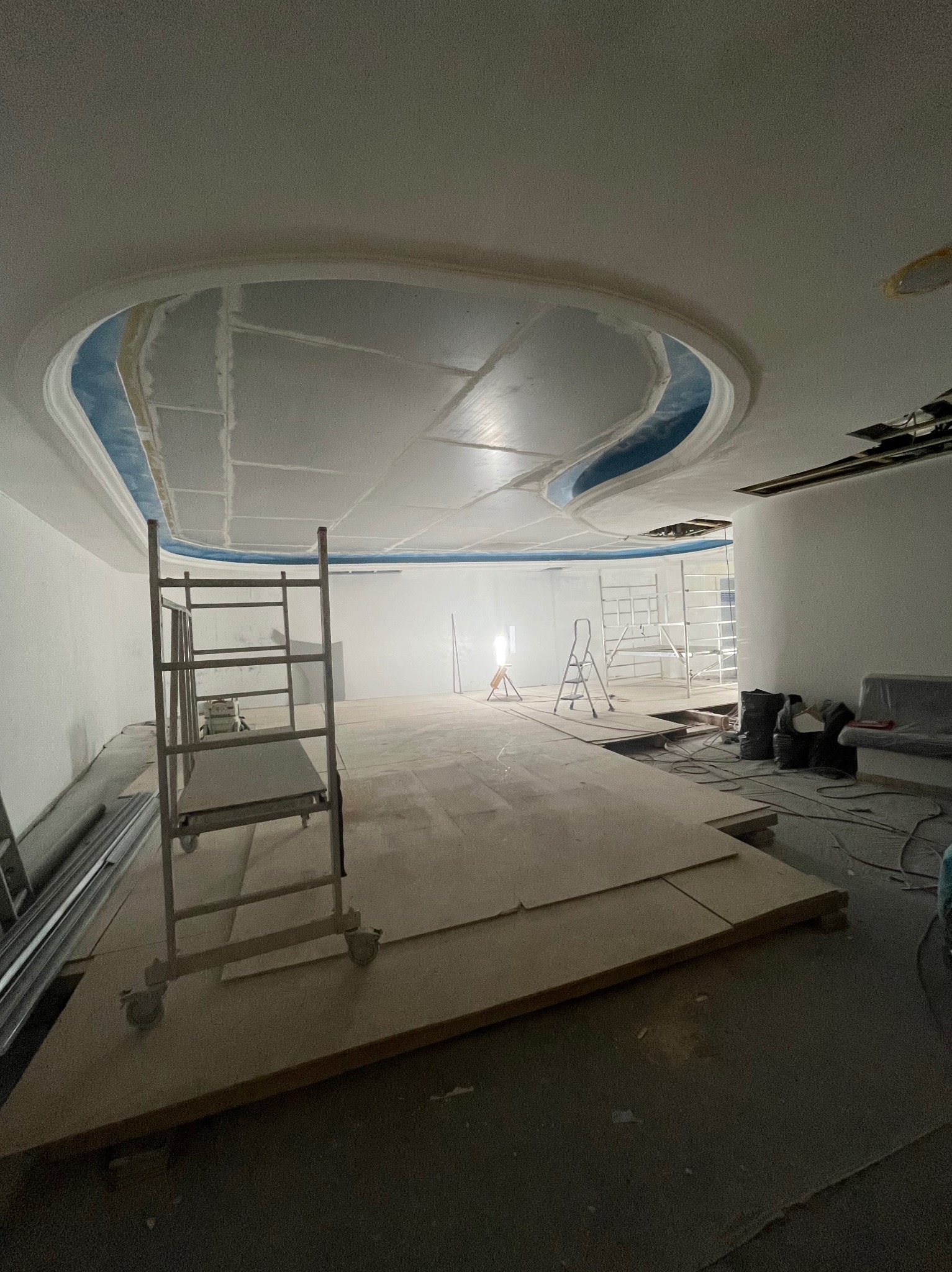 Wnętrze w trakcie prac wykończeniowych: podwieszany sufit z płyt karton-gips o nieregularnym kształcie, metalowe rusztowanie, przygotowanie do malowania.