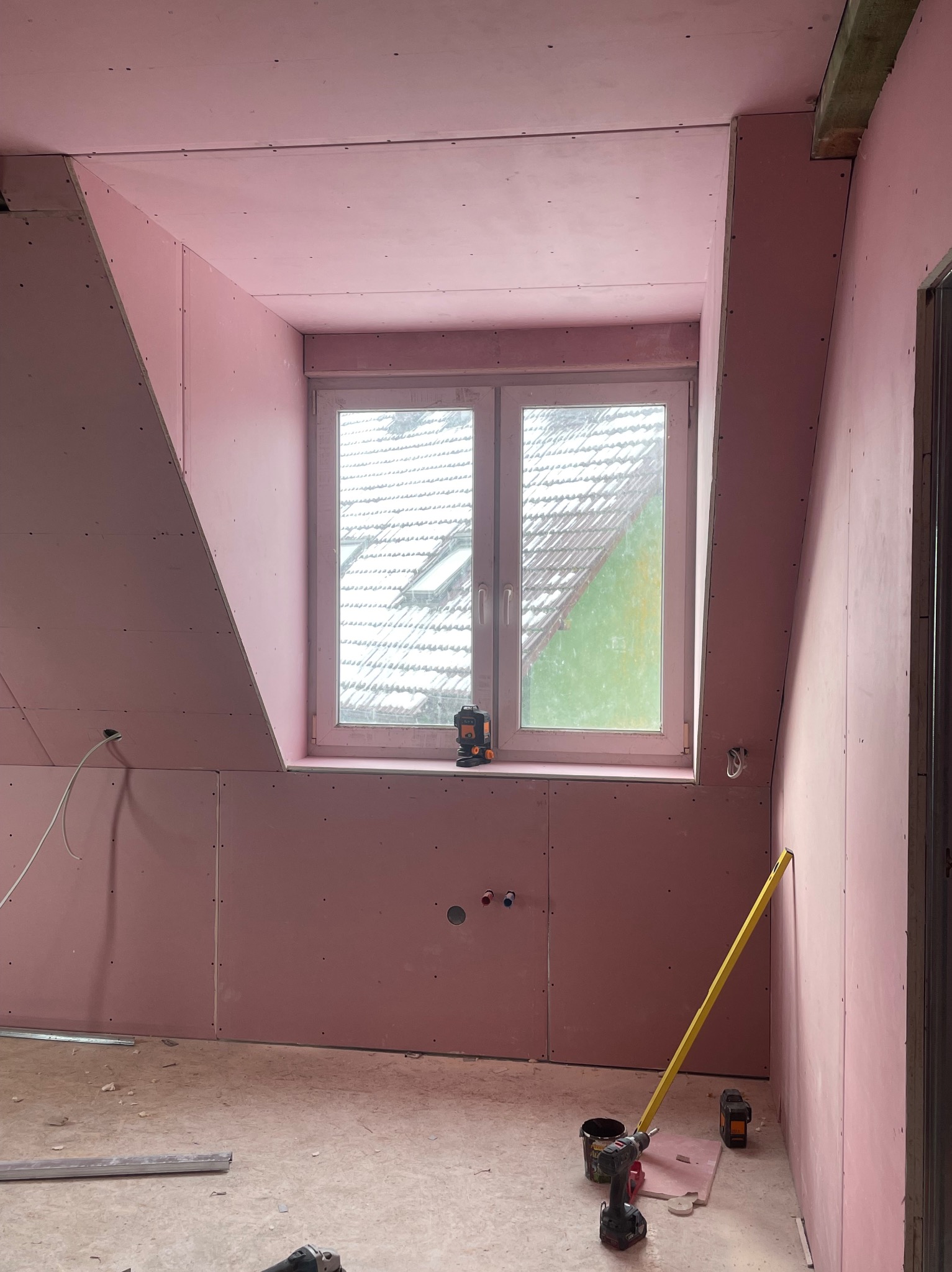 Montaż płyt gipsowo-kartonowych na poddaszu w Świnoujściu. Widoczne okno, poziomica i narzędzia. Prace wykończeniowe w trakcie realizacji.