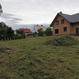 Uslugi Ogrodnicze Marcin Węgrzyn - Po koszeniu: trawa skoszona na posesji z domem w budowie w tle. Na pierwszym planie leży kosa spalinowa.