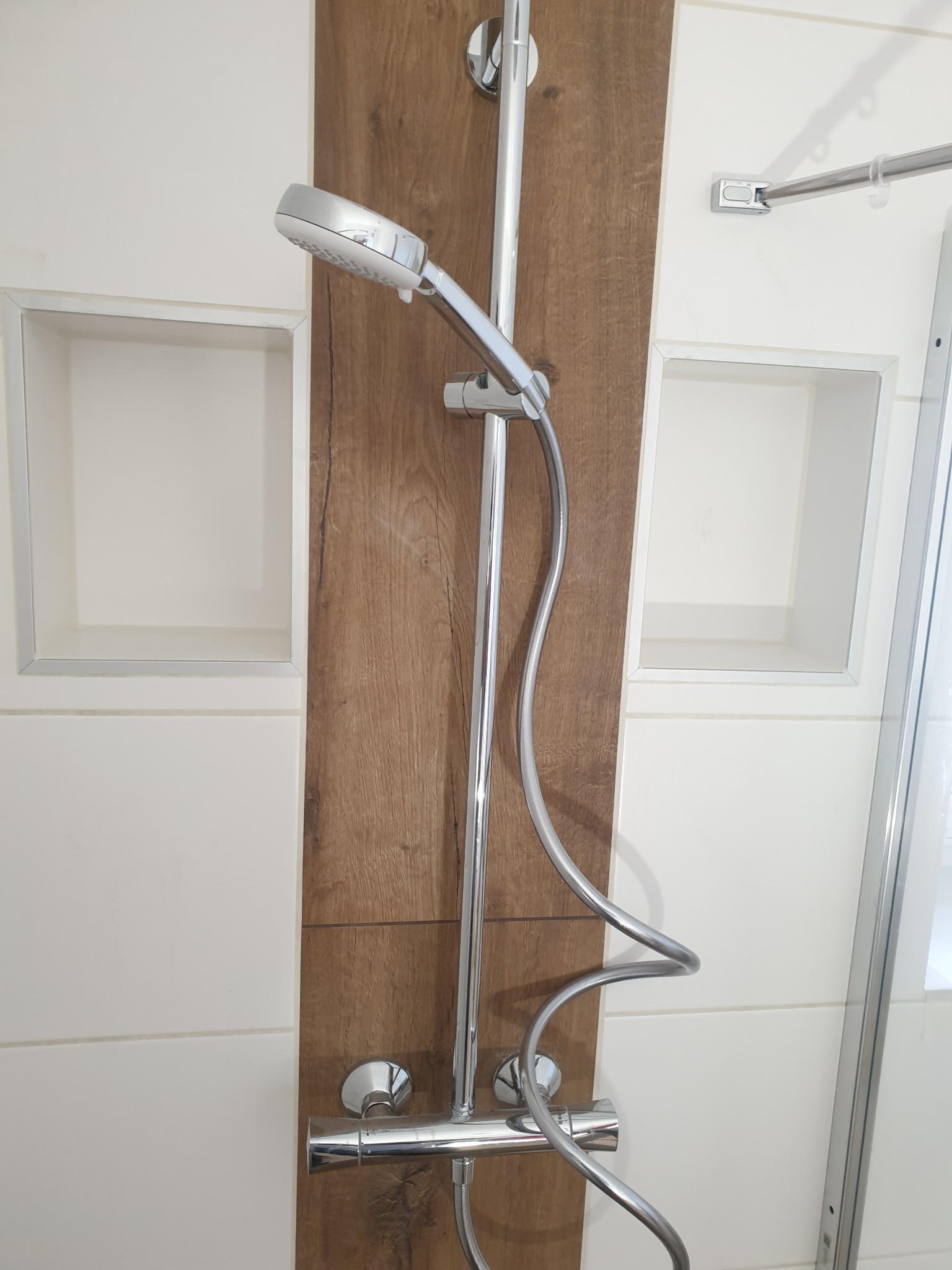 Chromowany zestaw natryskowy z deszczownicą na tle drewnopodobnej płyty w kabinie prysznicowej z wnękami, nowoczesny design.