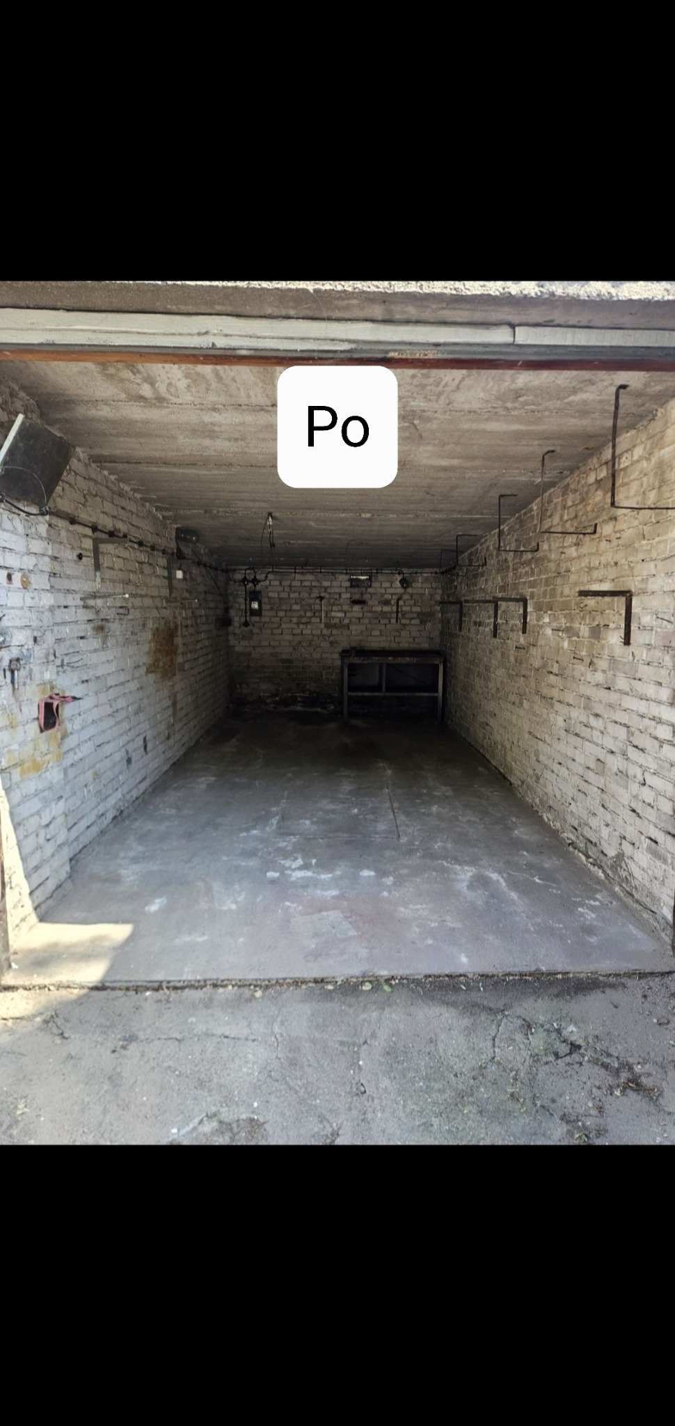 Wnętrze garażu po sprzątaniu: puste, z betonową podłogą i białymi ceglanymi ścianami. Widoczne instalacje na ścianach i suficie.