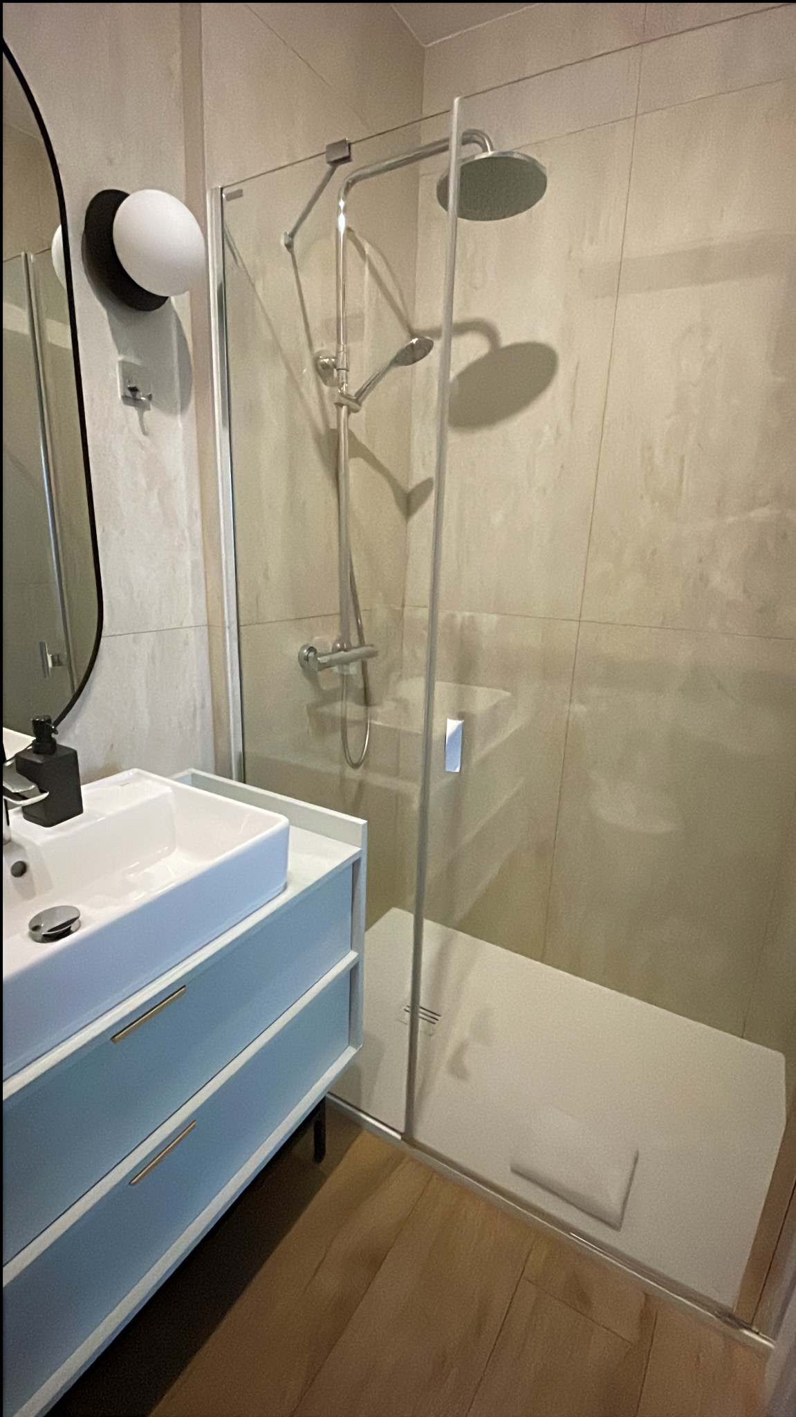 Nowoczesna łazienka z kabiną typu walk-in, umywalką na szafce w odcieniach błękitu i drewnianą podłogą. Minimalistyczny design, stonowana kolorystyka, oszczędne oświetlenie.