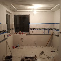 Tomasz Żabicki - Wnętrze łazienki w trakcie remontu: częściowo położone płytki z dekoracyjnym pasem, widoczne instalacje, przygotowane ściany i sufit pod dalsze prace wykończeniowe.