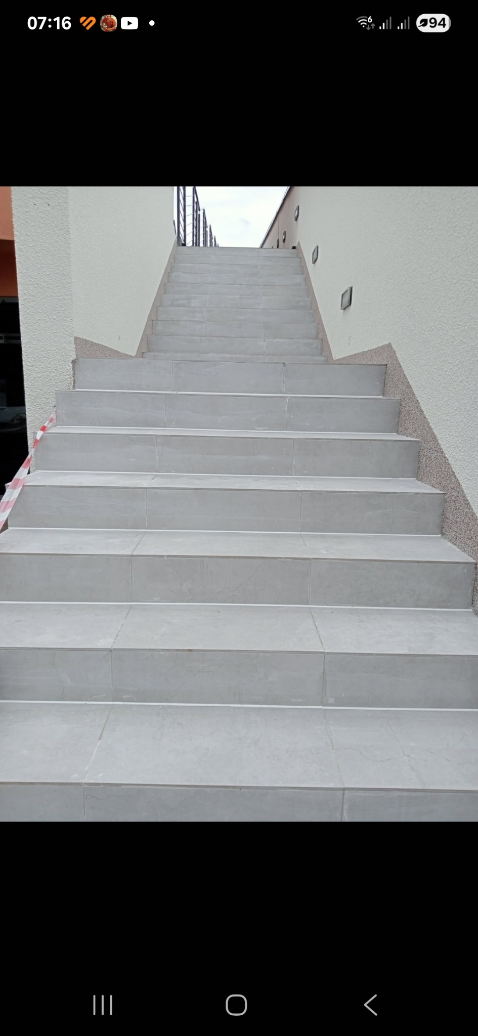 Wykończone, zewnętrzne schody z jasnoszarych płytek prowadzące do góry, z dekoracyjnym wykończeniem ścian w odcieniach beżu i brązu.