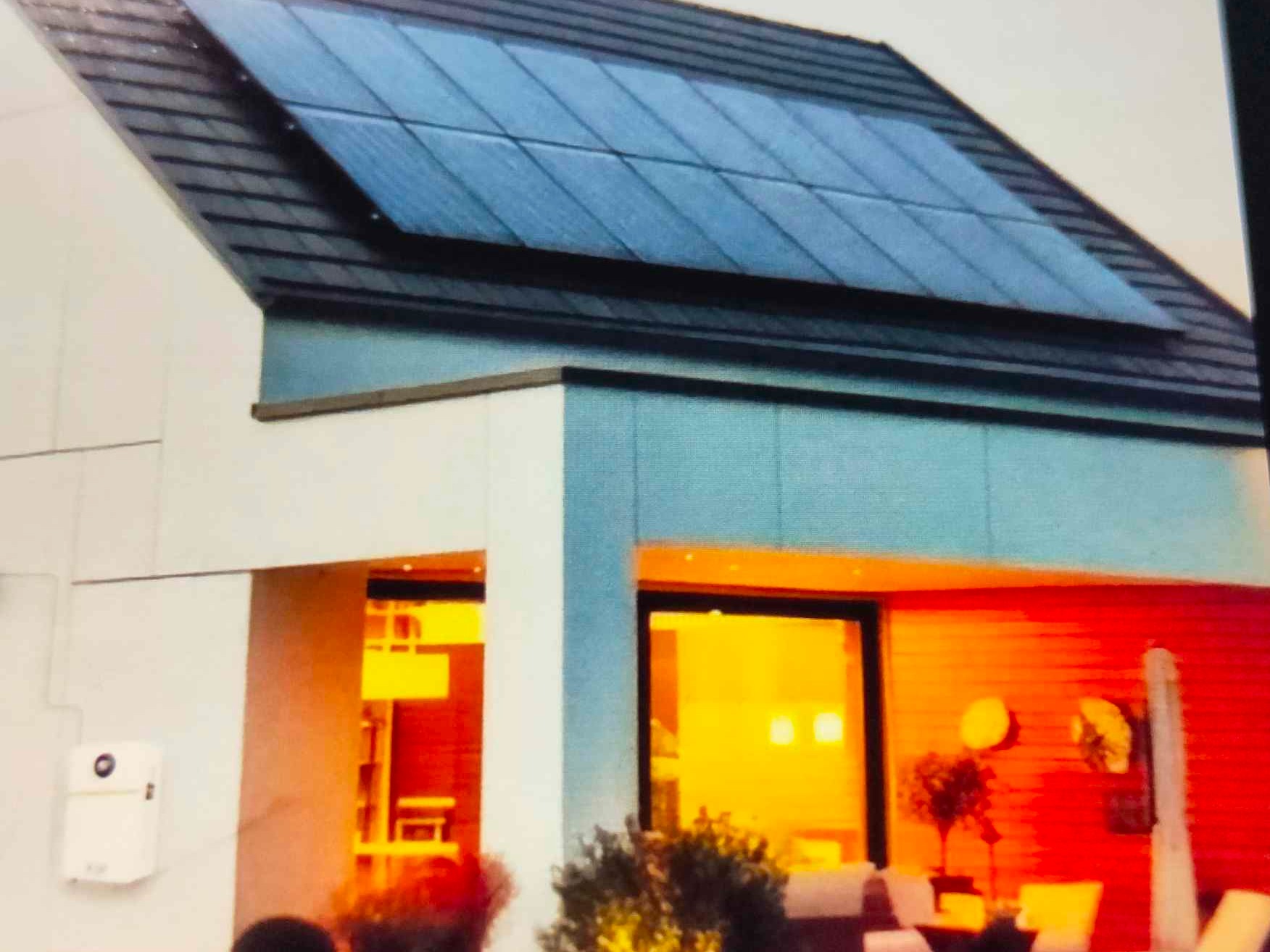 Nowoczesny dom z panelami słonecznymi na dachu, widok z zewnątrz. Czerwona ściana wewnątrz, oświetlenie ciepłym światłem. Biała elewacja i szare panele.