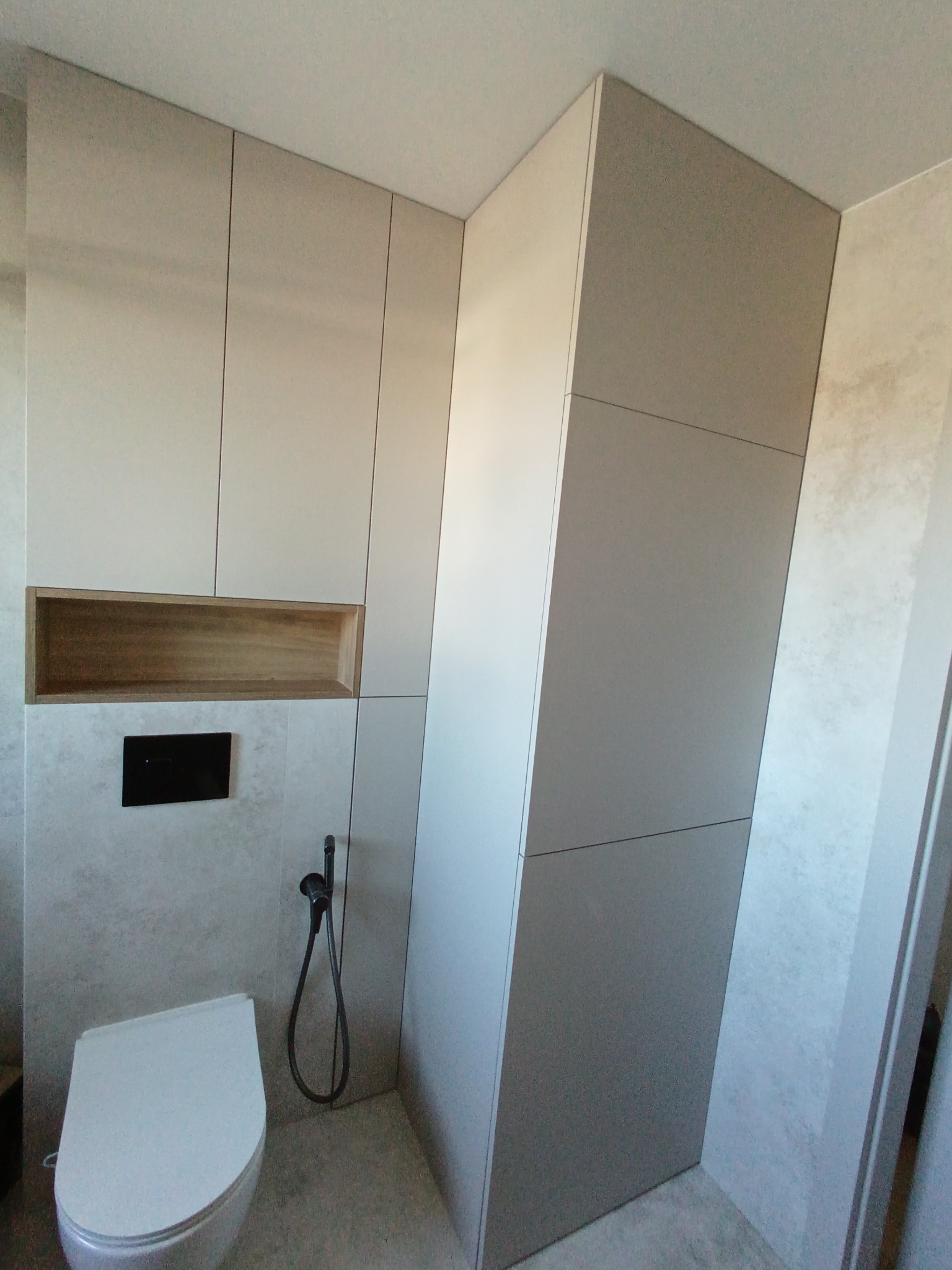 Nowoczesna łazienka z zabudową meblową w odcieniach szarości i beżu. Wisząca toaleta, drewniana wnęka i minimalistyczna armatura tworzą spójną całość.