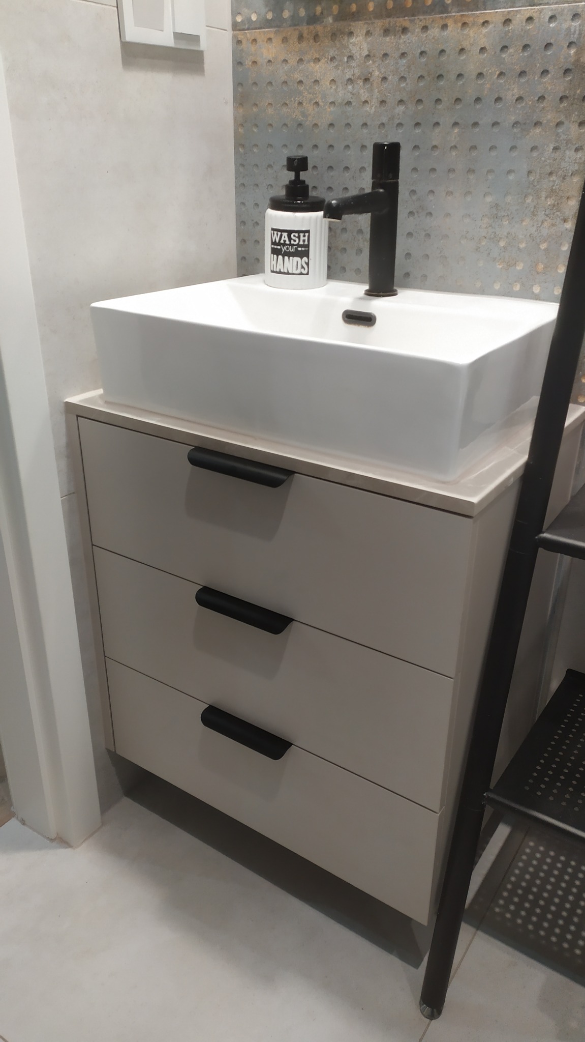 Nowoczesna szafka łazienkowa z trzema szufladami, umywalką nablatową i czarną armaturą. Minimalistyczny design, jasne kolory, dekoracyjna ściana w tle.