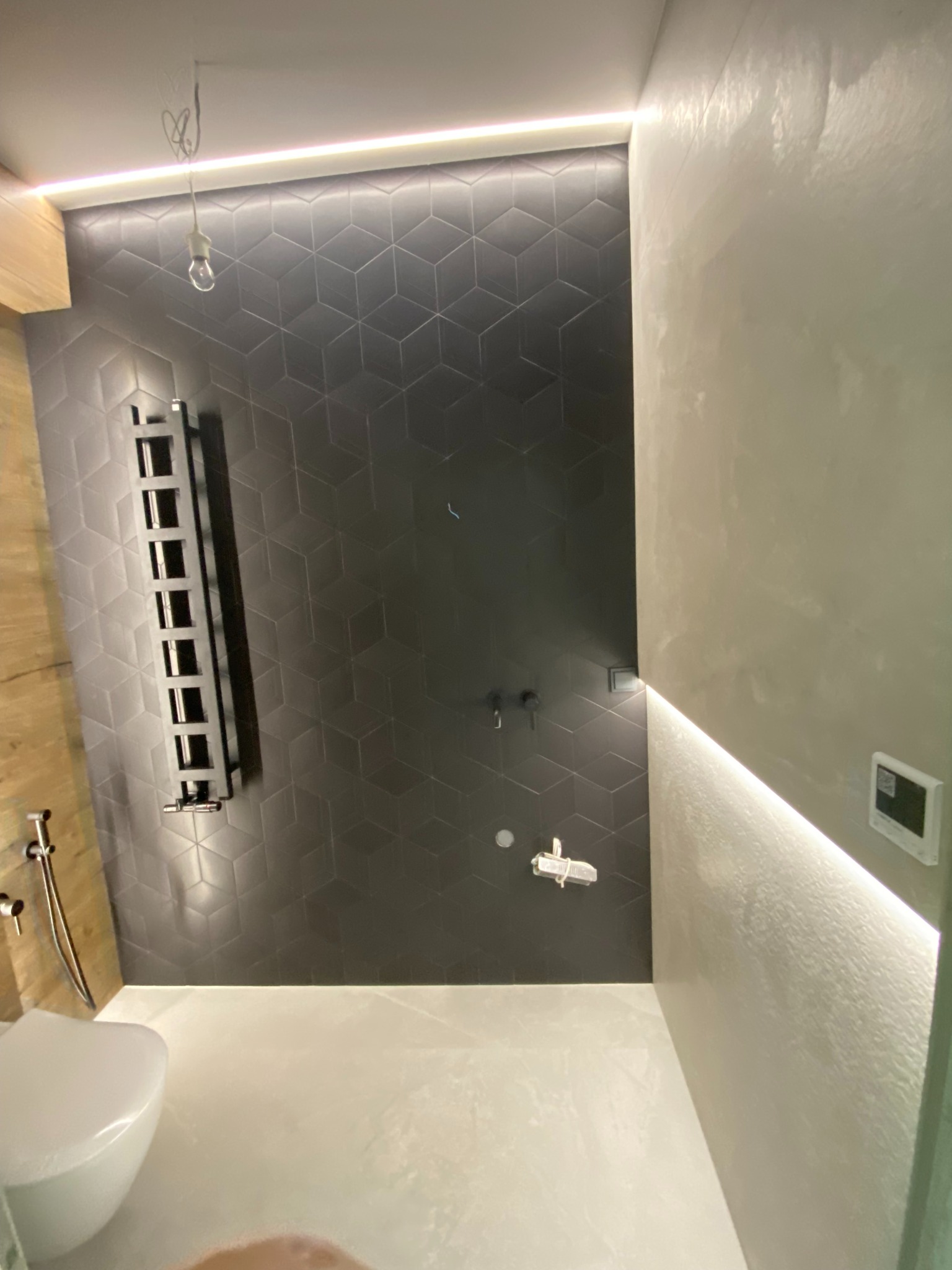 Nowoczesna łazienka po remoncie: heksagonalne płytki, grzejnik drabinkowy i oświetlenie LED. Minimalistyczny design z elementami drewna i armaturą.