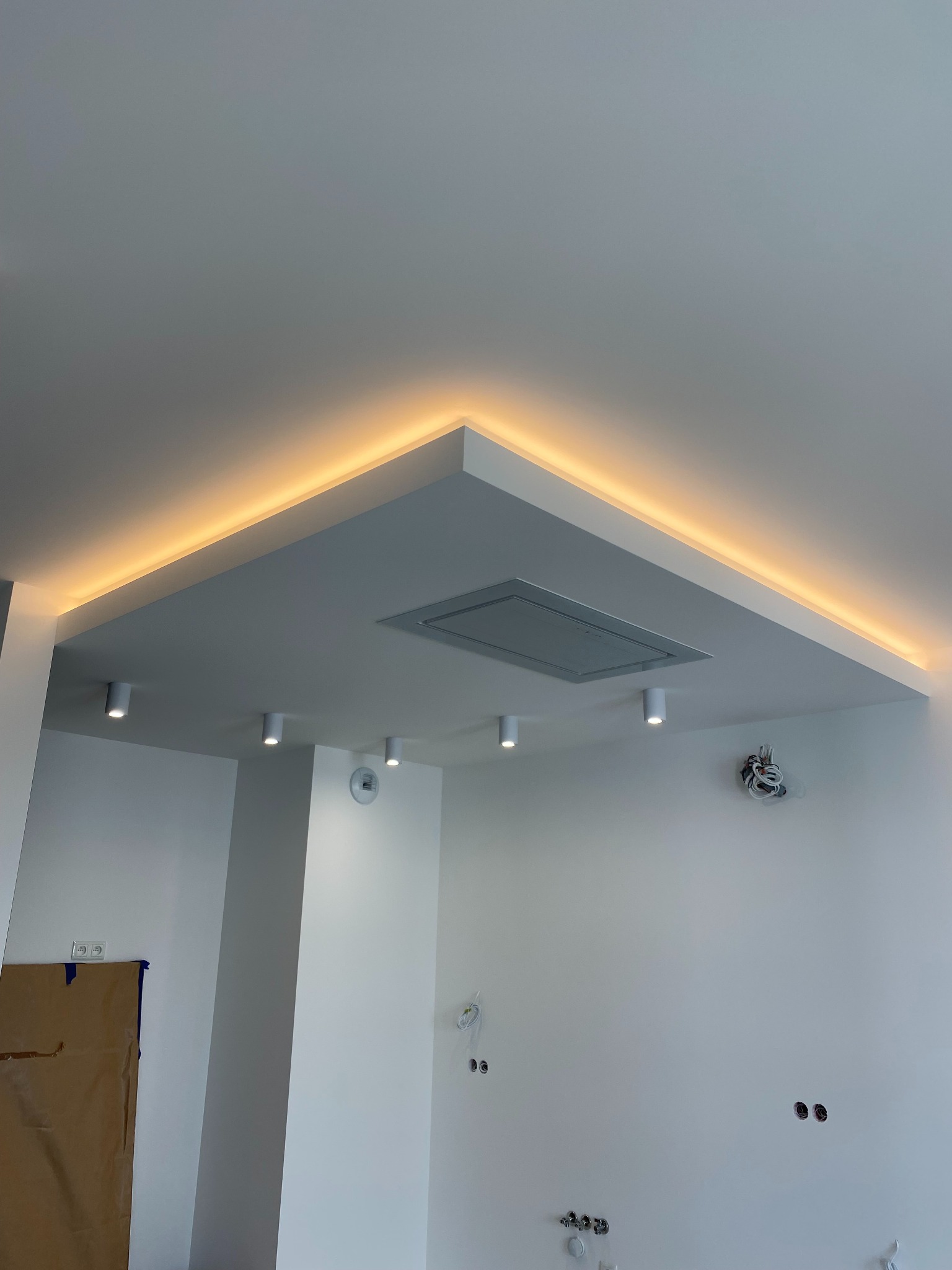 Nowoczesny sufit podwieszany z oświetleniem LED w ciepłym odcieniu, w minimalistycznym wnętrzu z białymi ścianami i punktowymi lampami.