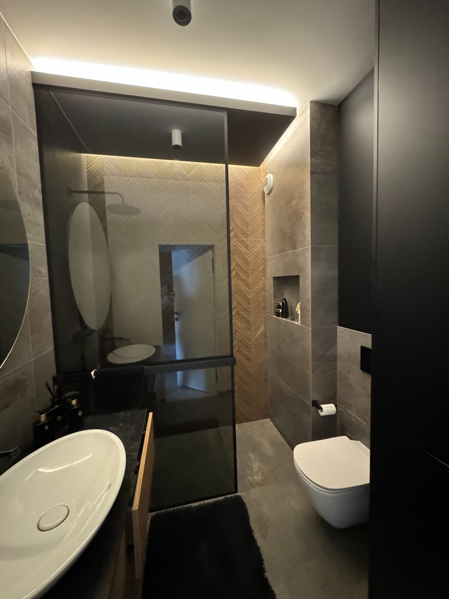 Nowoczesna łazienka z kabiną prysznicową typu walk-in, umywalką nablatową i toaletą. Grafitowe szafki i płytki w odcieniach szarości tworzą elegancki wystrój.