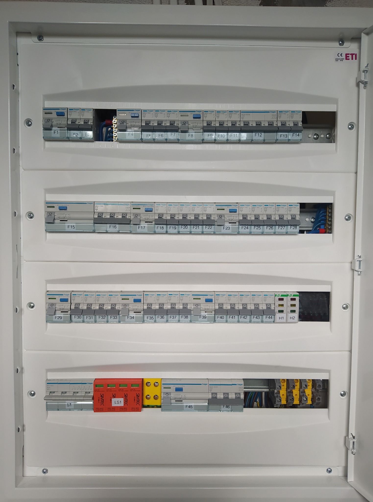 Otwarta skrzynka bezpiecznikowa z zainstalowanymi bezpiecznikami i przewodami, widok z bliska. Instalacja elektryczna wewnątrz pomieszczenia.