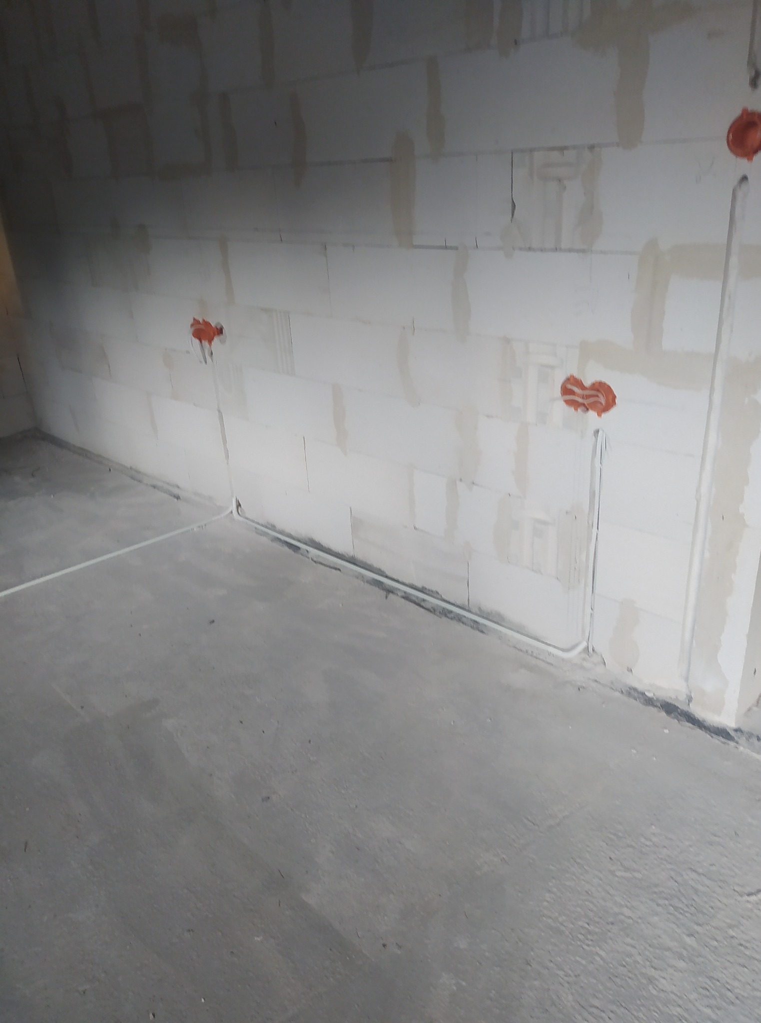 Wewnętrzne okablowanie w surowym pomieszczeniu z białymi ścianami z betonu komórkowego i widocznymi puszkami instalacyjnymi oraz przewodami podtynkowymi.