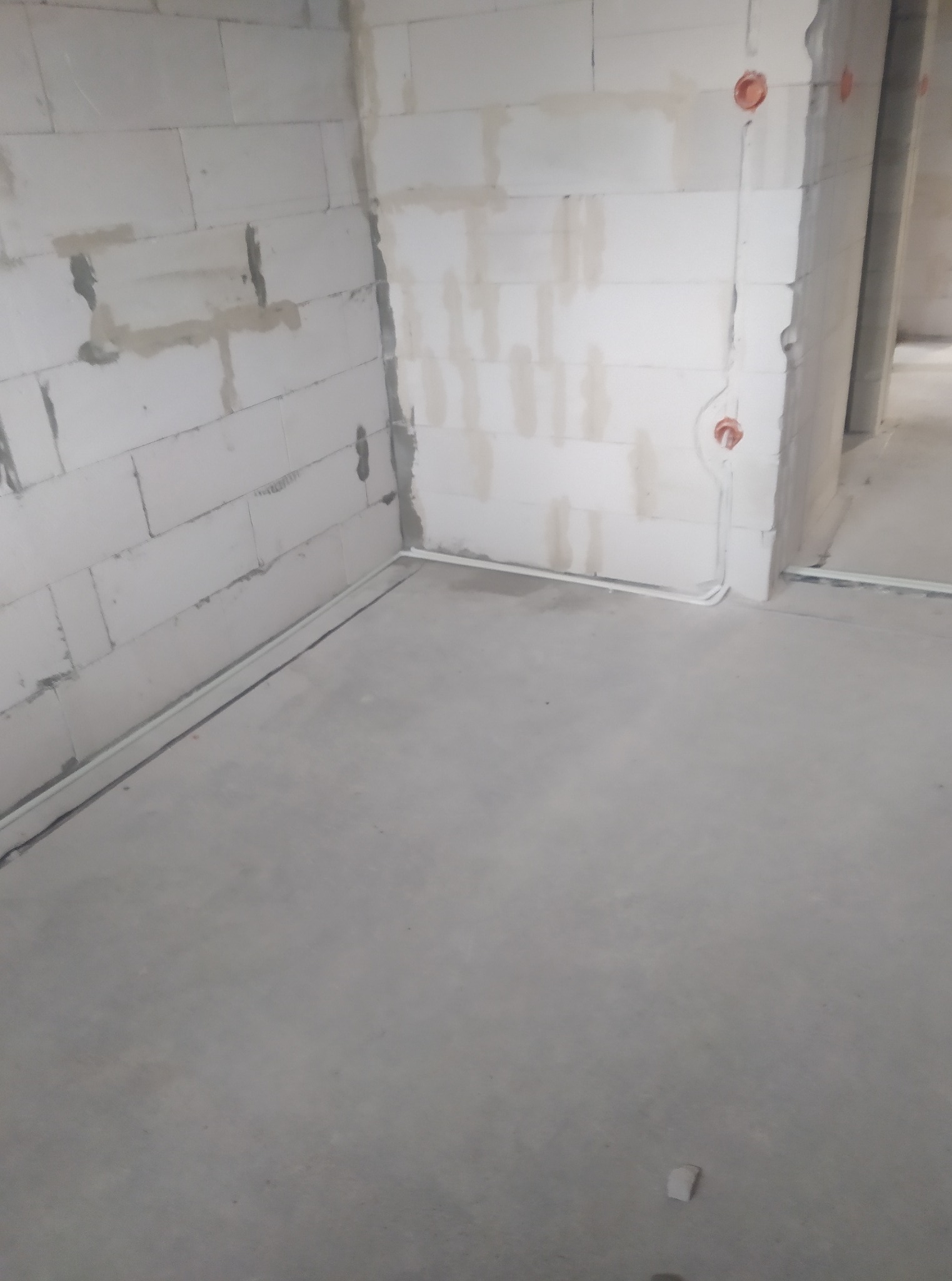Wnętrze w trakcie prac. Widoczne przewody elektryczne poprowadzone wzdłuż ścian i puszki instalacyjne w ścianach z betonu komórkowego. Surowy stan wykończenia.