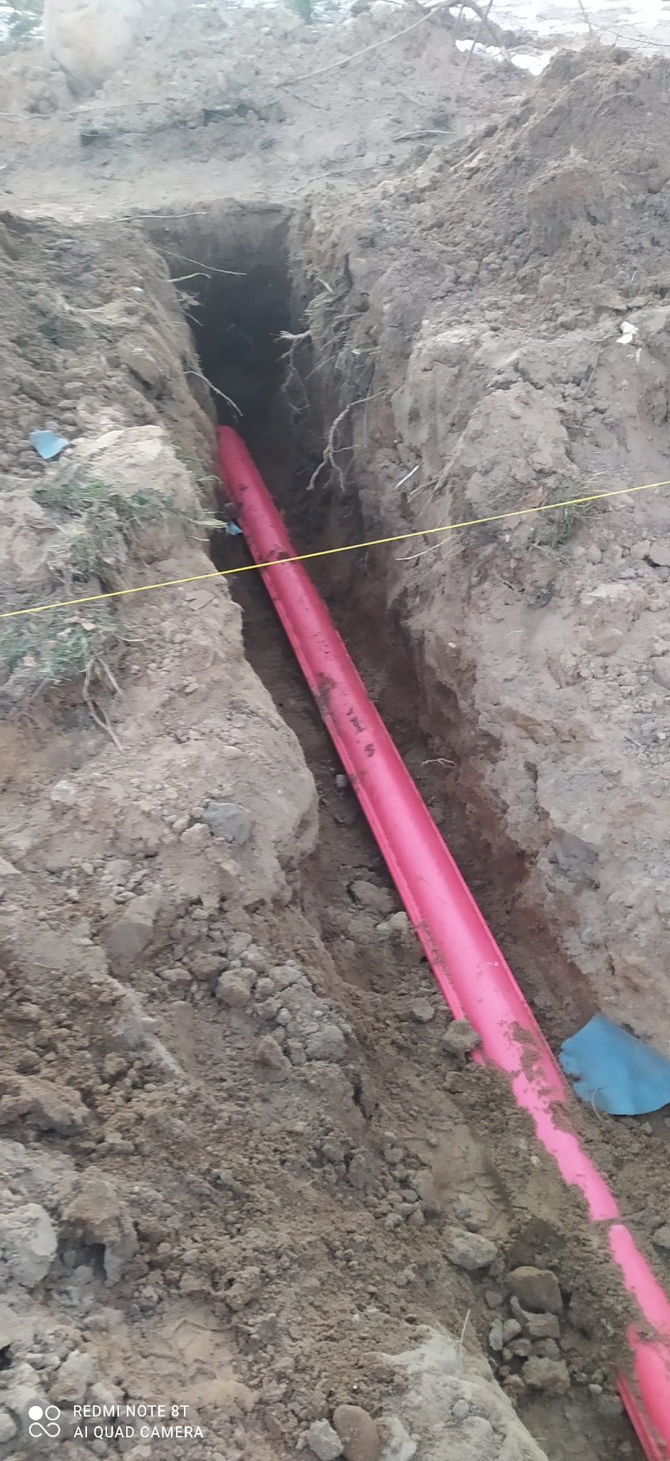 Różowa rura kablowa ułożona w wykopie ziemnym, zabezpieczona przed uszkodzeniami mechanicznymi. Żółta linka wyznacza trasę przebiegu.