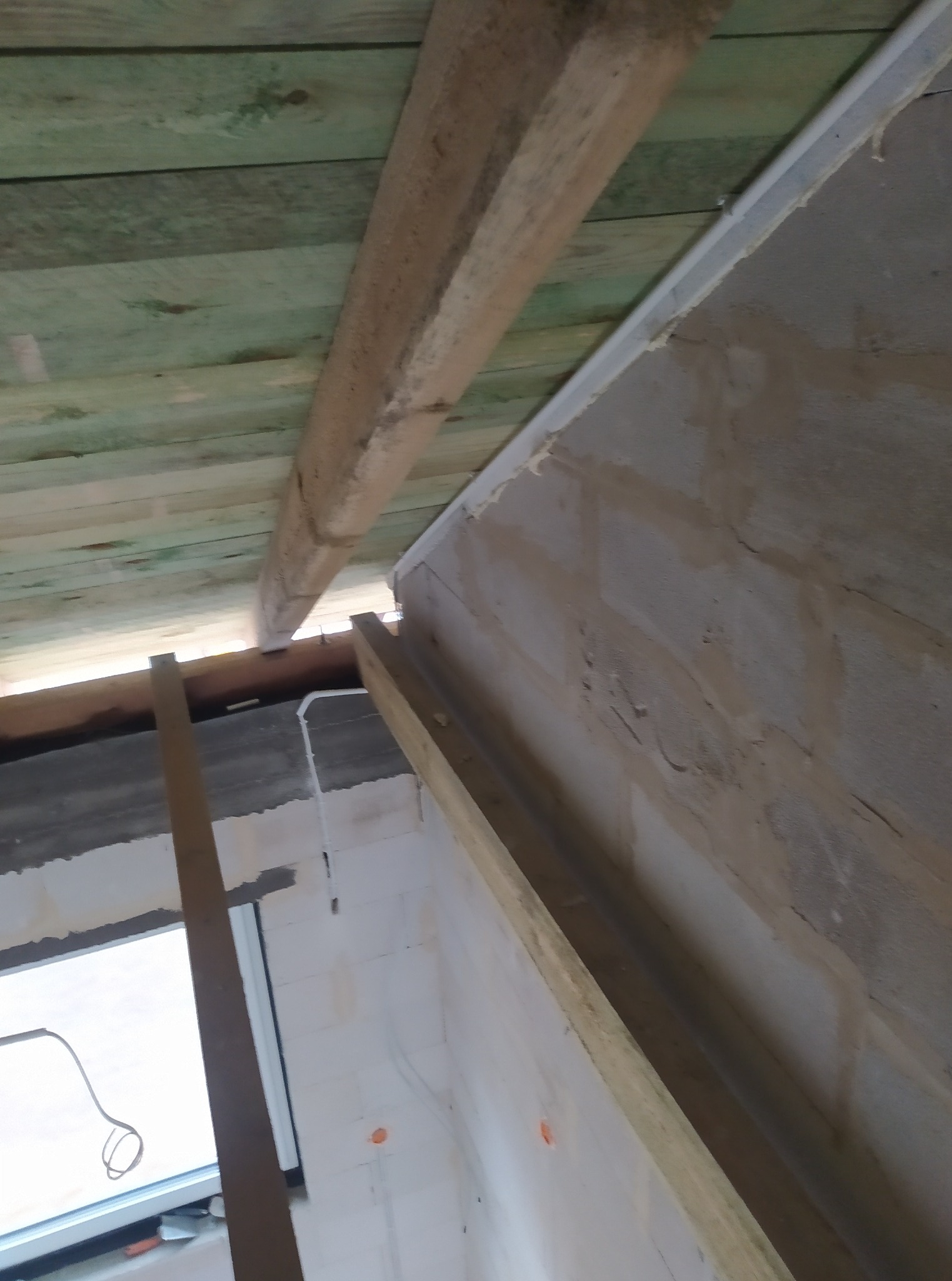 Surowy strop z drewnianymi belkami i fragmentem ściany z instalacją elektryczną w trakcie prac wykończeniowych. Widok z dołu.