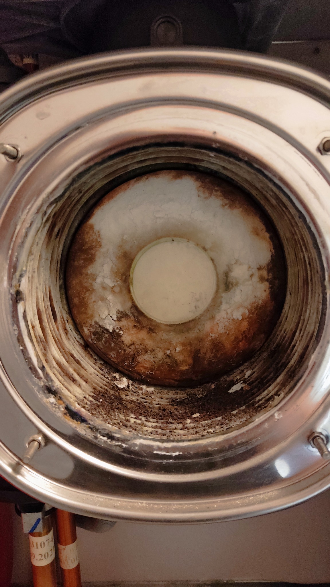 Wnętrze zardzewiałego, metalowego elementu pieca gazowego z osadem i zabrudzeniami, widok z góry.