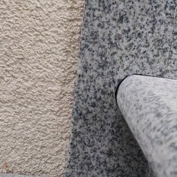 IVITECH - Fragment elewacji z tynkiem barankiem i szarą okładziną kamienną z zaokrąglonym elementem. Detal wykończenia zewnętrznego budynku.