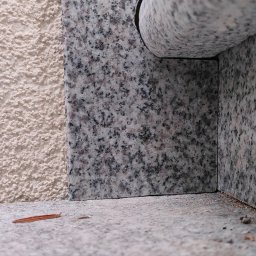 IVITECH - Detale wykończenia elewacji: połączenie szorstkiego tynku w odcieniu beżu i płyt z szarego, nakrapianego granitu. Widoczny narożnik i fragment parapetu.