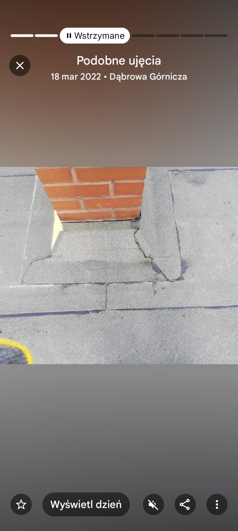 Szczegółowe ujęcie obróbki blacharskiej komina na dachu pokrytym papą. Widoczne łączenia i uszczelnienia wokół ceglanego komina.