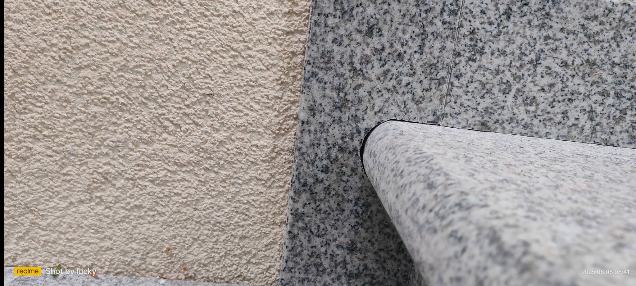 Fragment elewacji z tynkiem barankiem i szarą okładziną kamienną z zaokrąglonym elementem. Detal wykończenia zewnętrznego budynku.