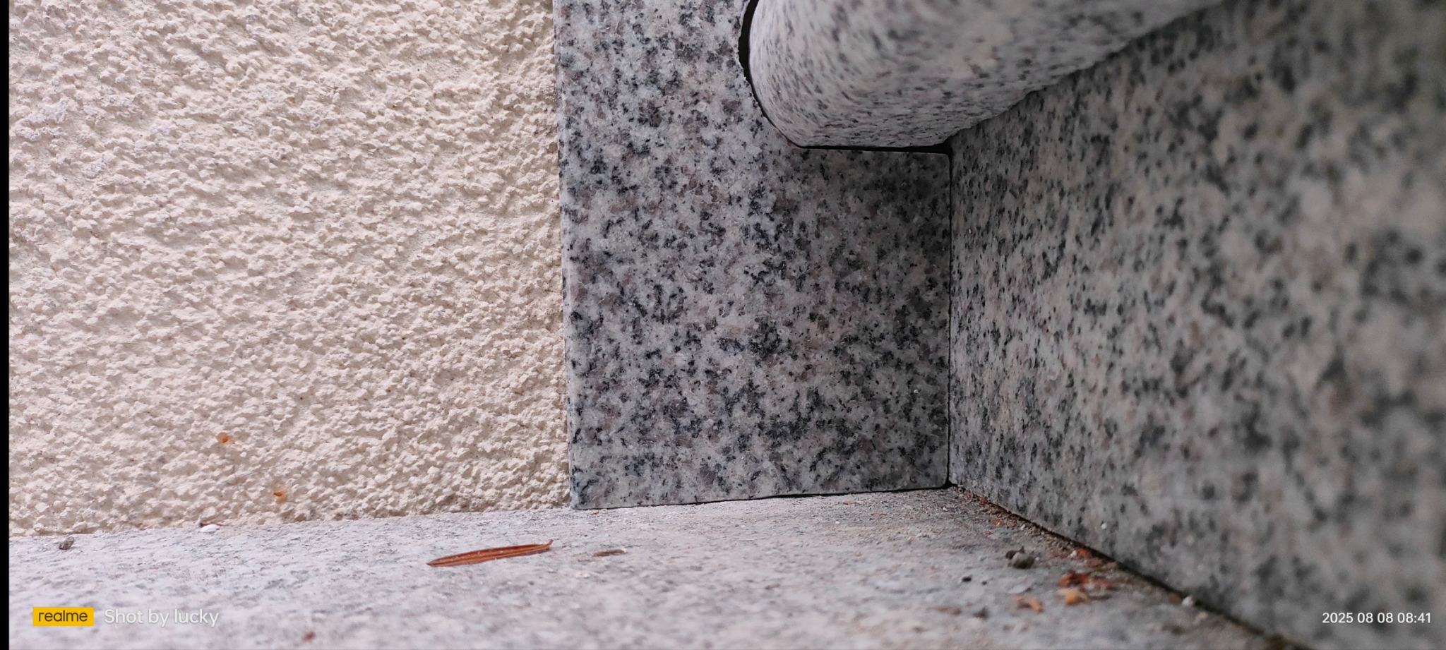 Detale wykończenia elewacji: połączenie szorstkiego tynku w odcieniu beżu i płyt z szarego, nakrapianego granitu. Widoczny narożnik i fragment parapetu.