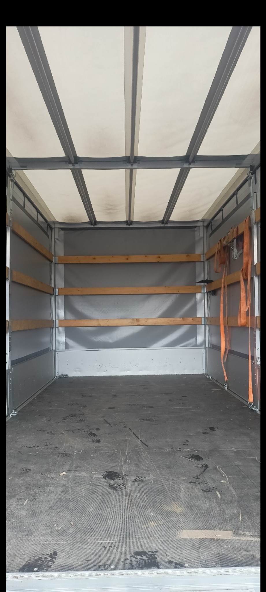 Wnętrze paki busa transportowego z drewnianymi listwami zabezpieczającymi ładunek i pasami mocującymi, widok z tyłu pojazdu.