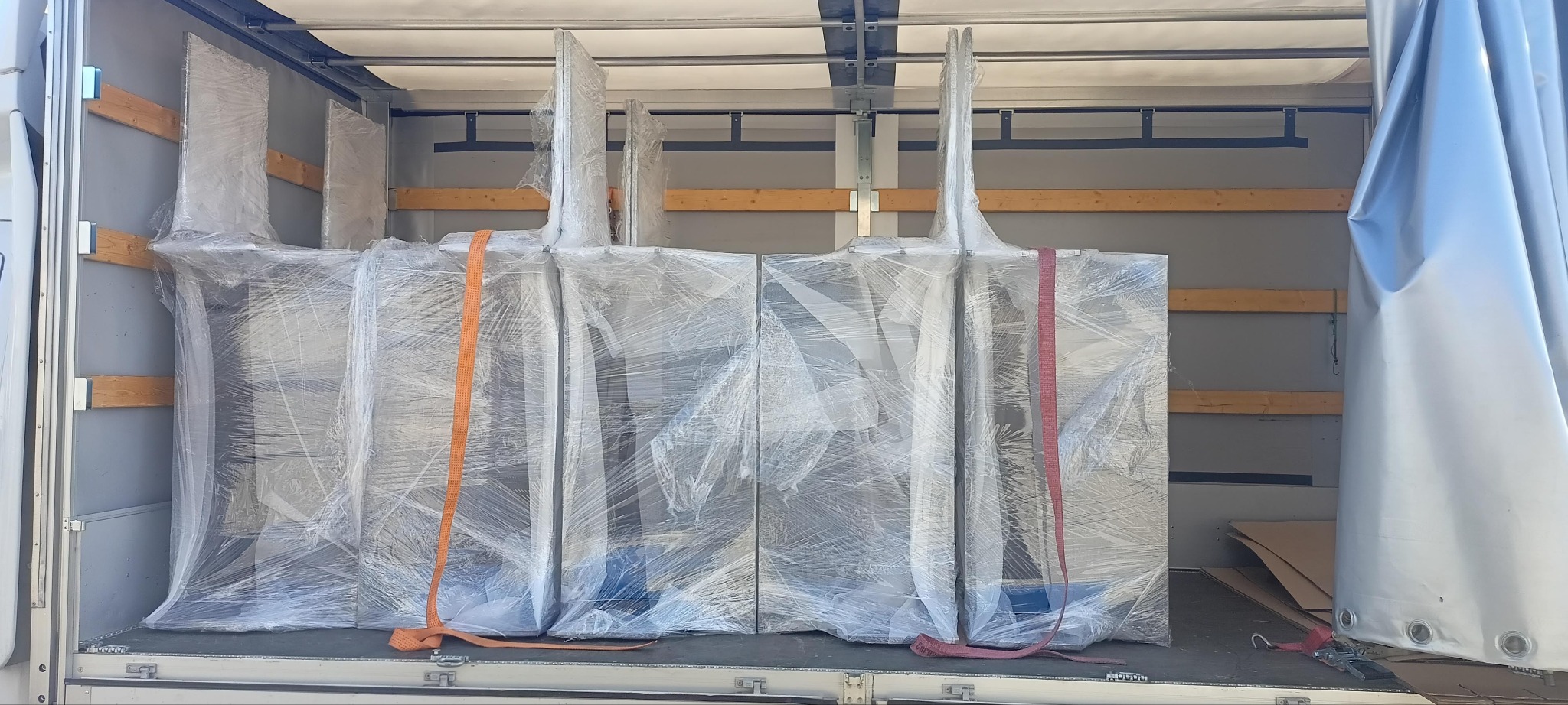 Zabezpieczone folią i pasami meble wewnątrz przestrzeni ładunkowej busa transportowego, gotowe do przewozu. Widoczne drewniane listwy mocujące.