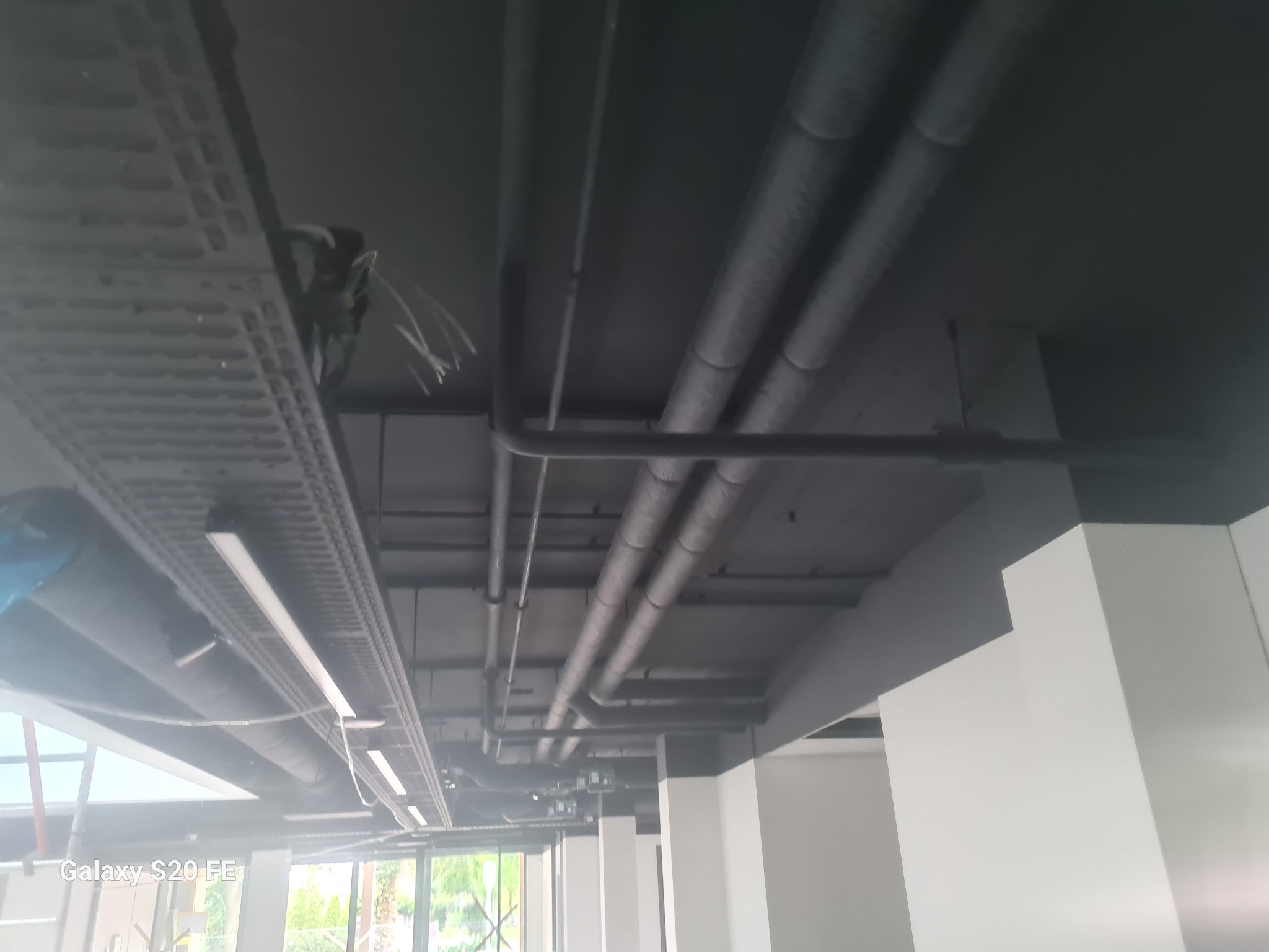 Szare rury instalacyjne pod sufitem w nowoczesnym wnętrzu, widoczne kable w korycie kablowym. Ujęcie z dołu, widok na instalacje.